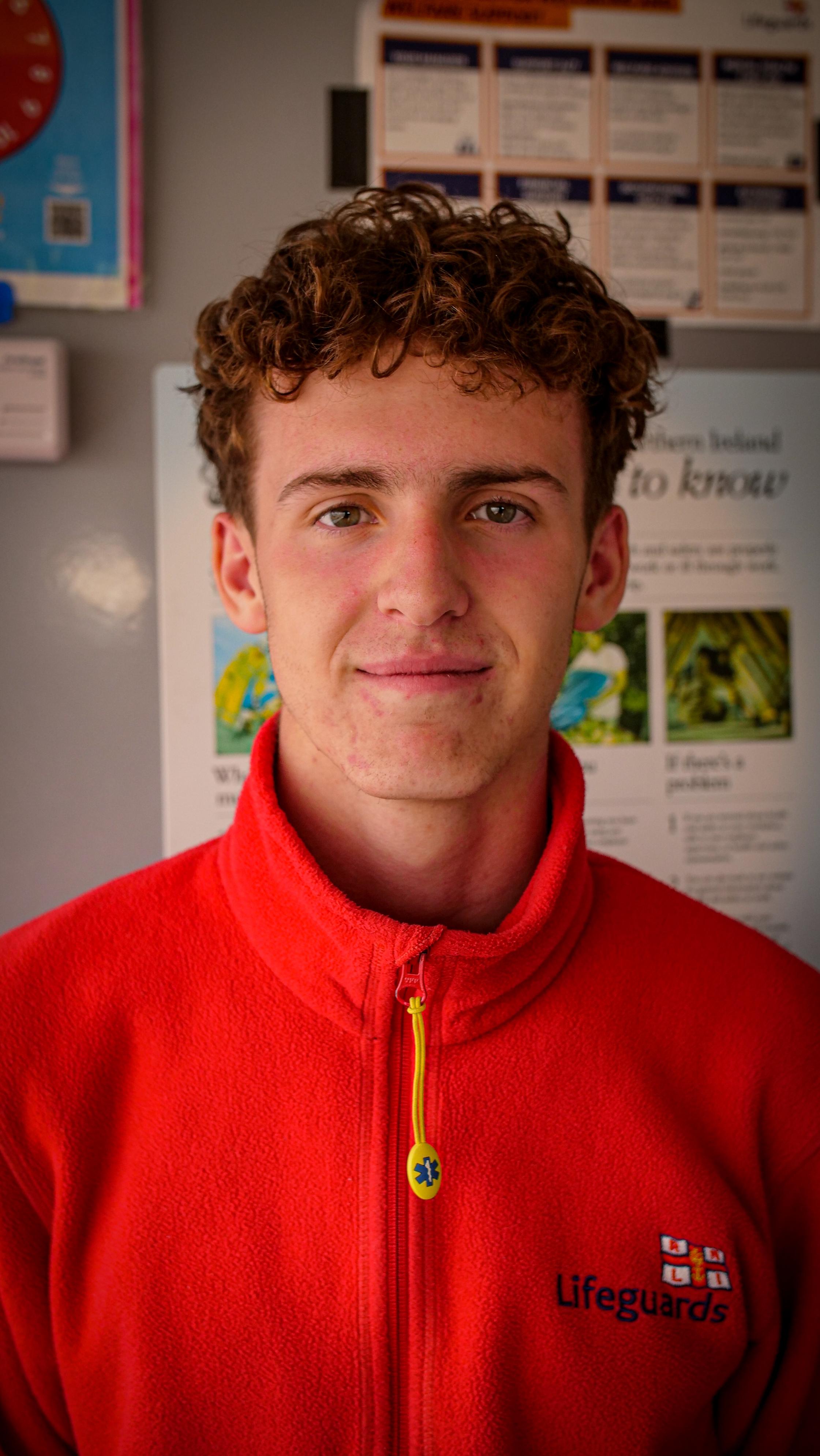 Lifeguard Cohan smiling at the camera in his red Lifeguard jumper 