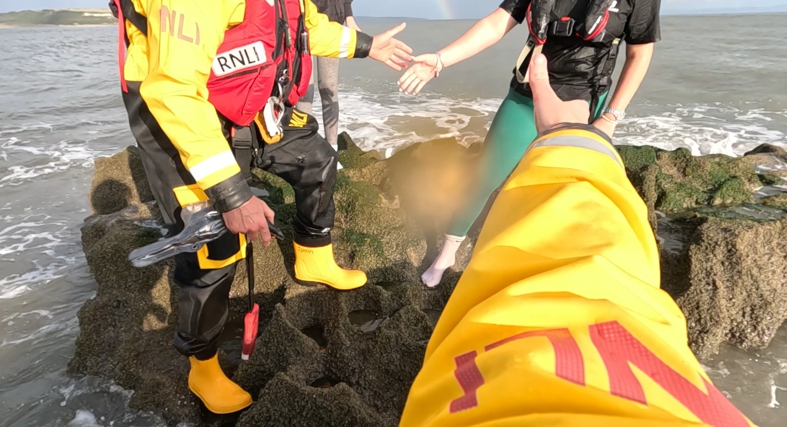 RNLI crew on rock helping one casualtie to climb onto ILB