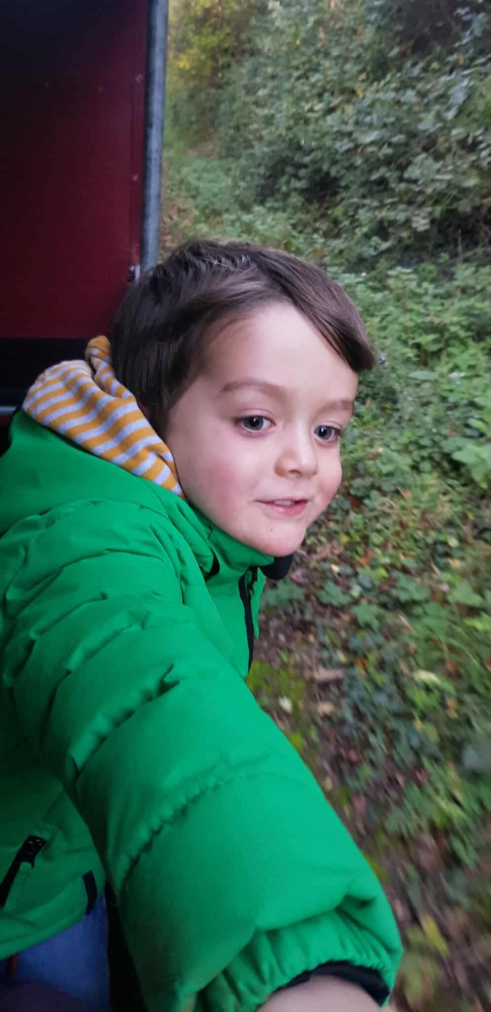 Sam in a green coat leaning and looking out of the train carriage smiling 