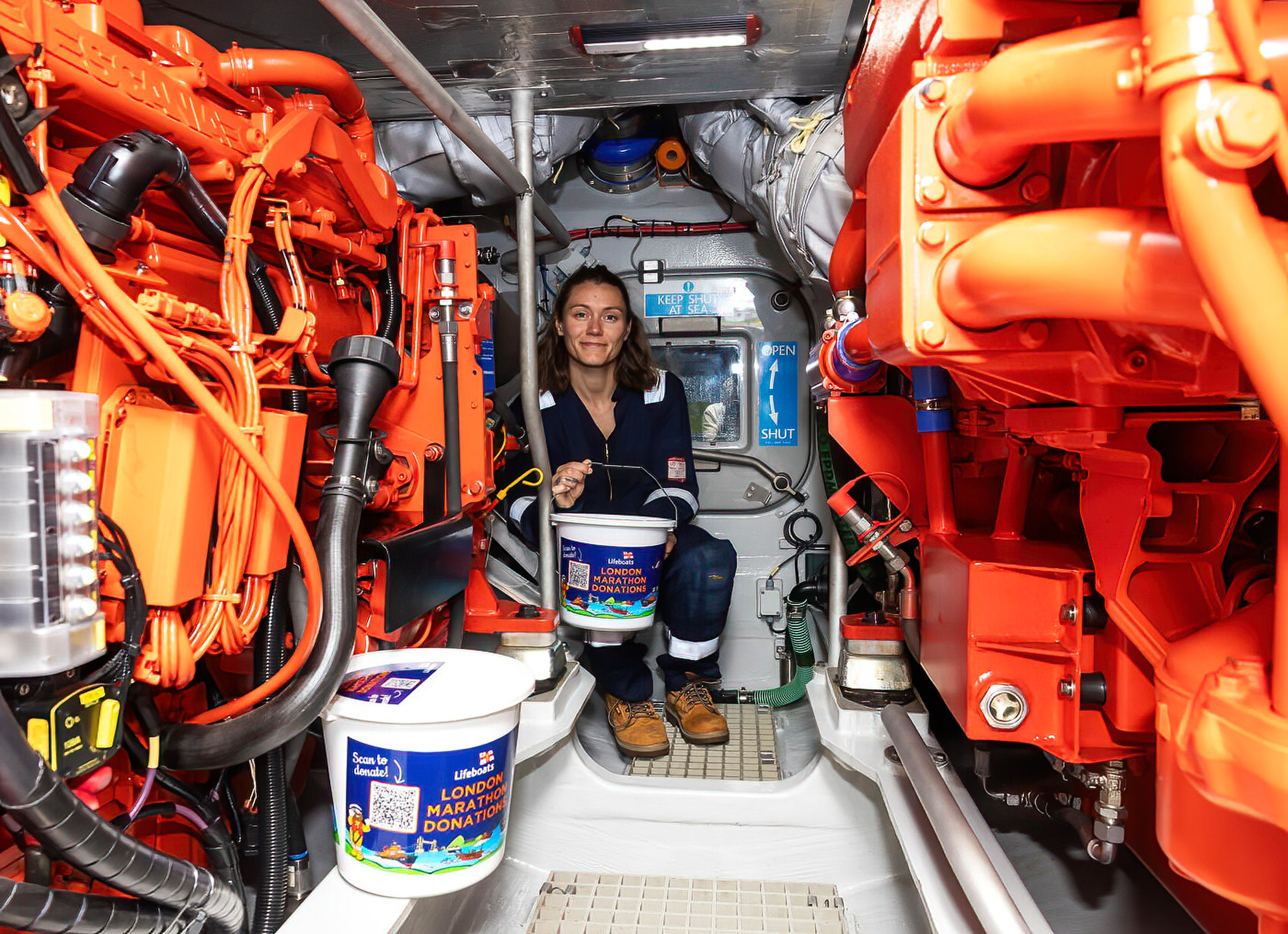 Jasmin in her blue boiler suit in the engine space on the Shannon surrounded by orange pipework
