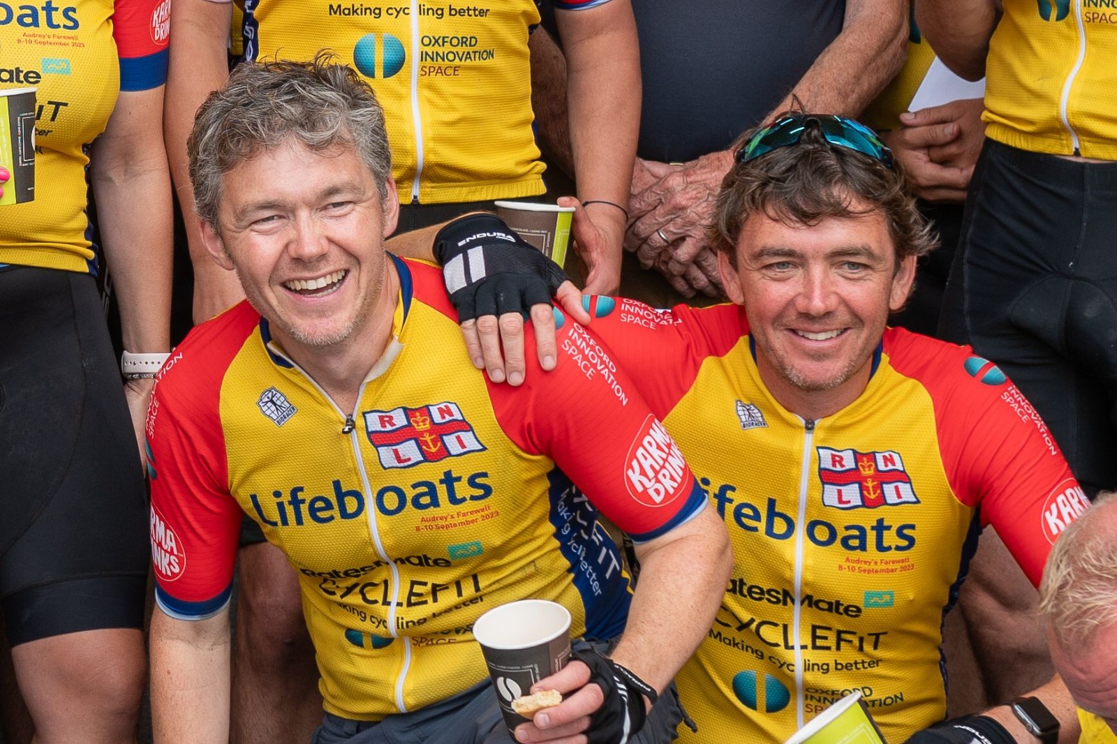Two men in lifeboat cycling jerseys celebrating their mammoth achievement. 