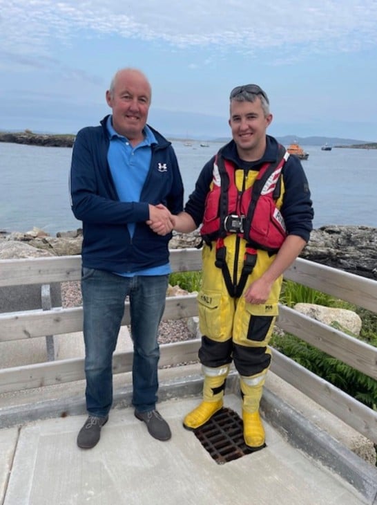 Father and son Sean and Kieran O'Donnell from Arranmore RNLI shaking hands with the lifeboat in the water in the background