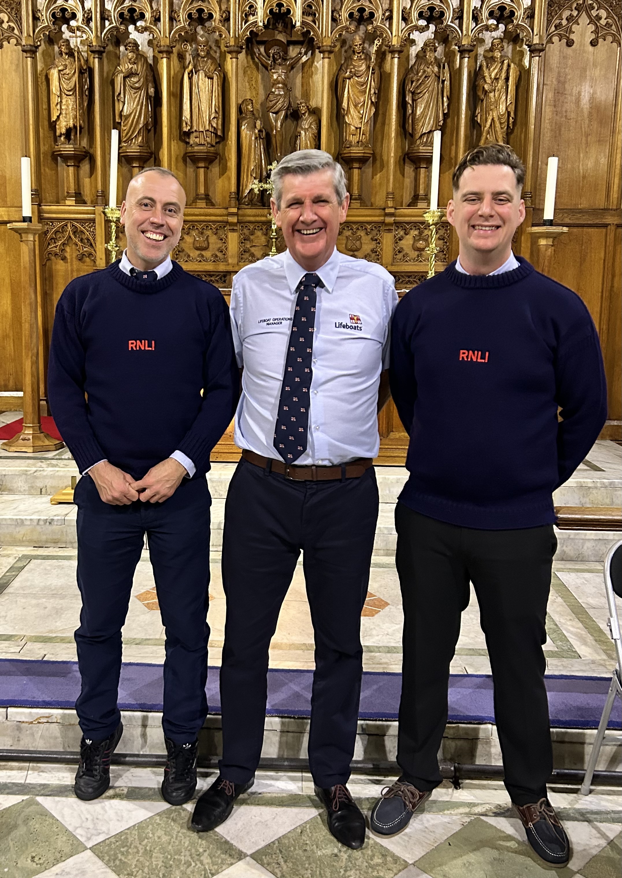 The photo shows 2 crew and the operations manager standing side by side in the church at the carol service
