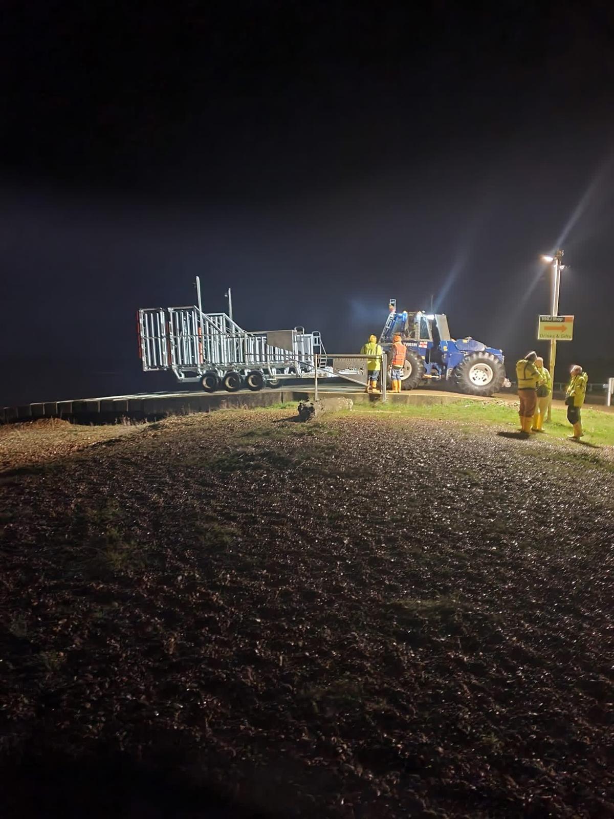 A group of RNLI volunteers around the large tractor and carriage at night after the lifeboat has launched on service