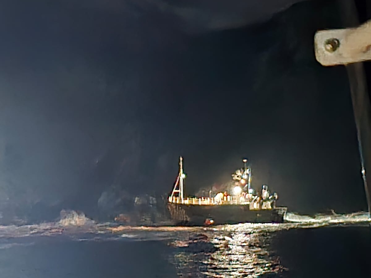 Aground guard vessel near rocks in darkness with lights on from the side