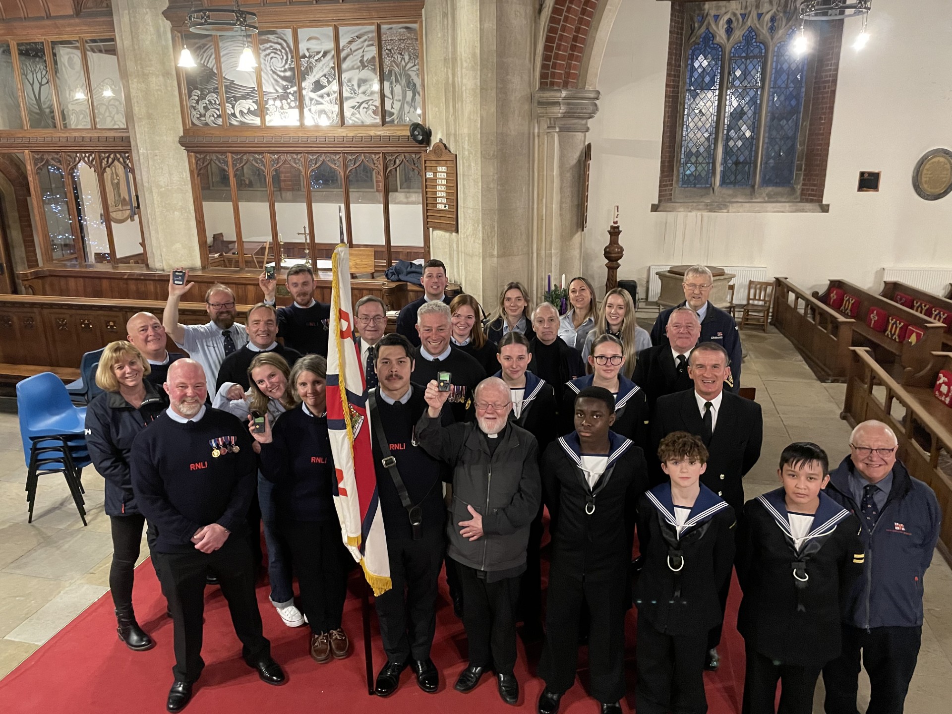 Volunteer crew and the lifeboat chaplain raise their pagers in salute of those on watch at Christmas. Crew are accompanied by Portsmouth Sea Cadets, who supported during the carol service