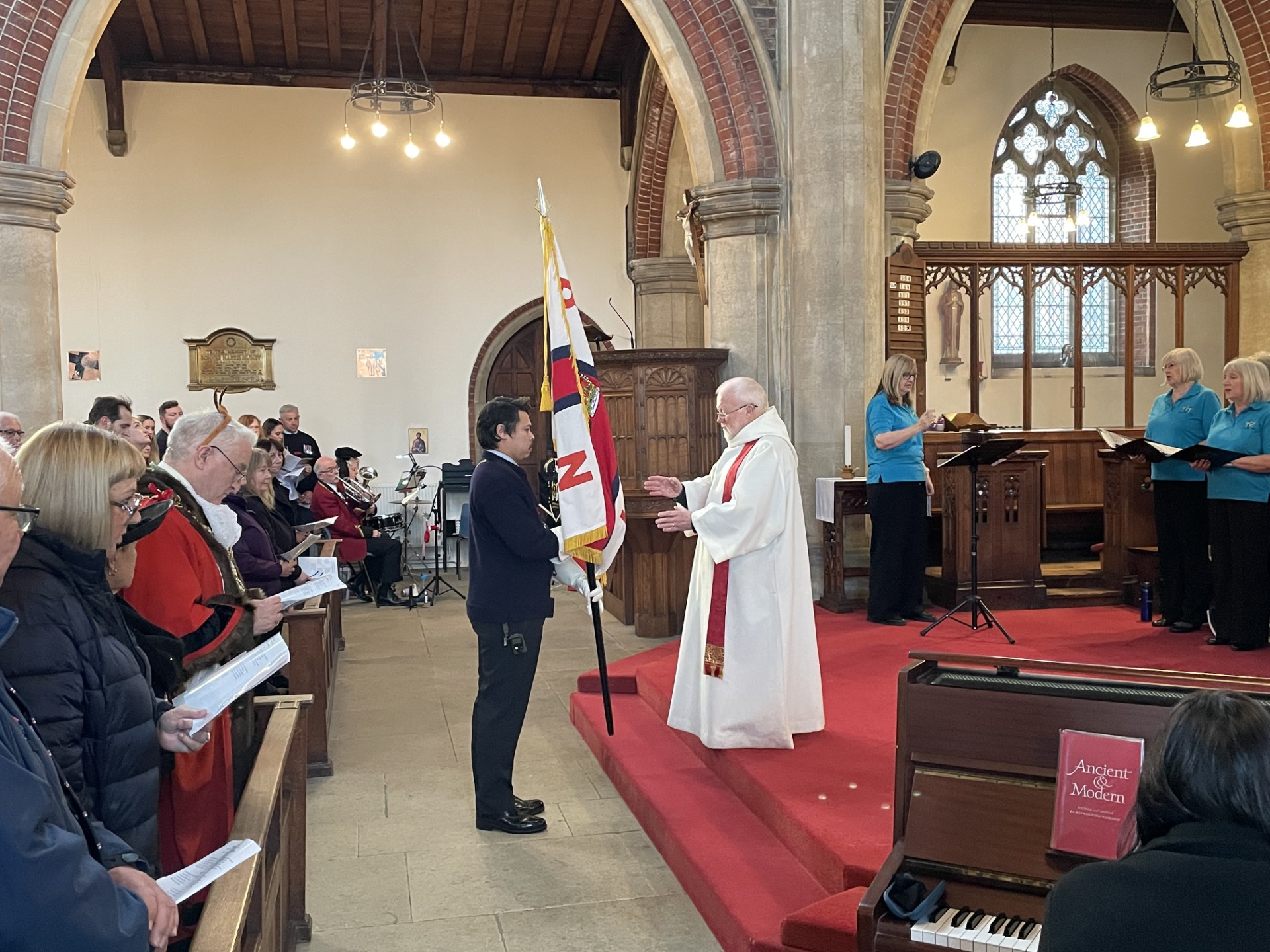 Fr John Strain, Portsmouth Lifeboat Chaplain, receives the standard from Crewmember Josh Owens to mark the start of the annual carol service