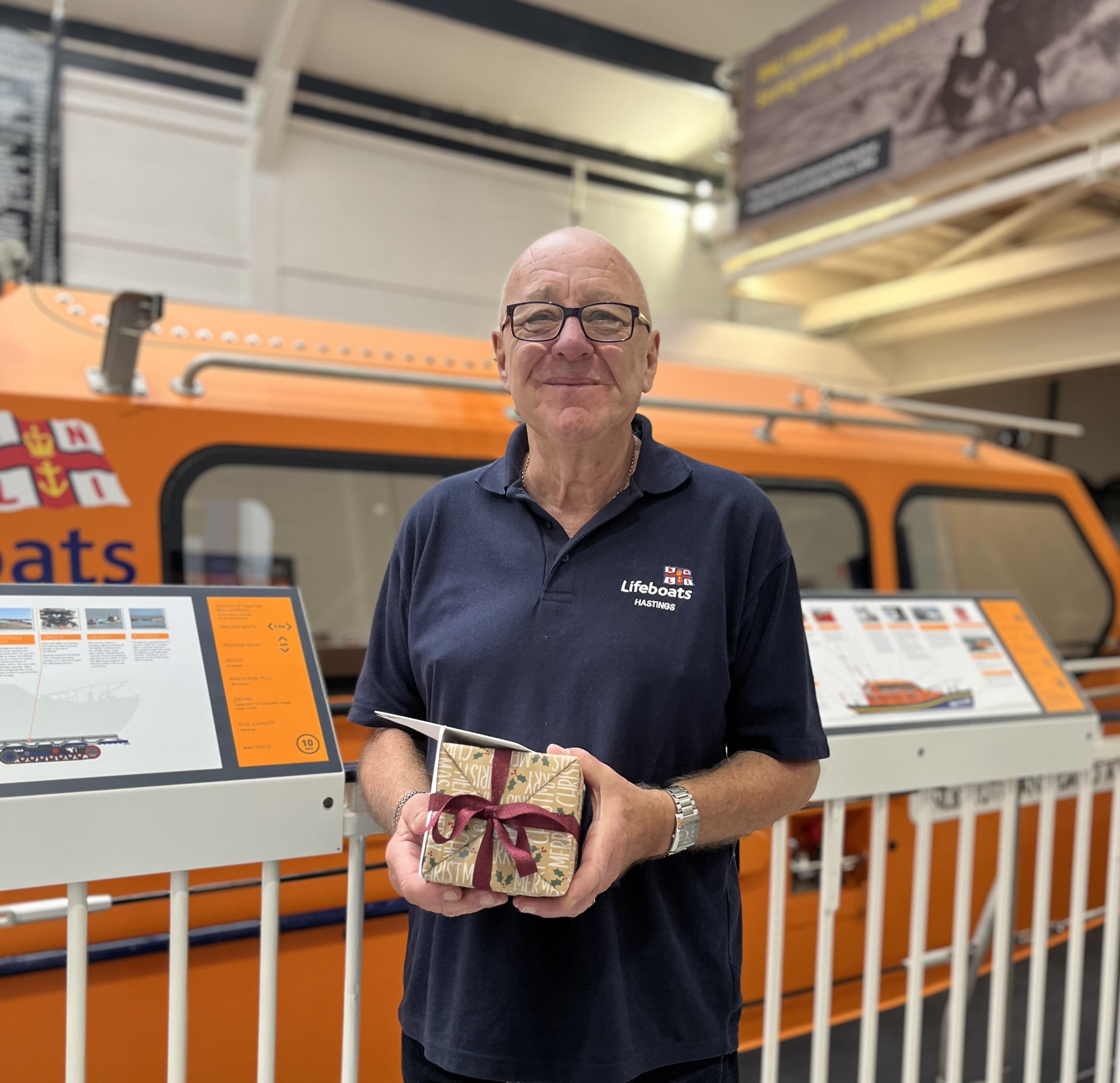 Arthur Miller, standing on the visitors gantry at Hastings lifeboat station, by the Shannon lifeboat. Arthur is holding a retirement gift presented by fellow volunteers