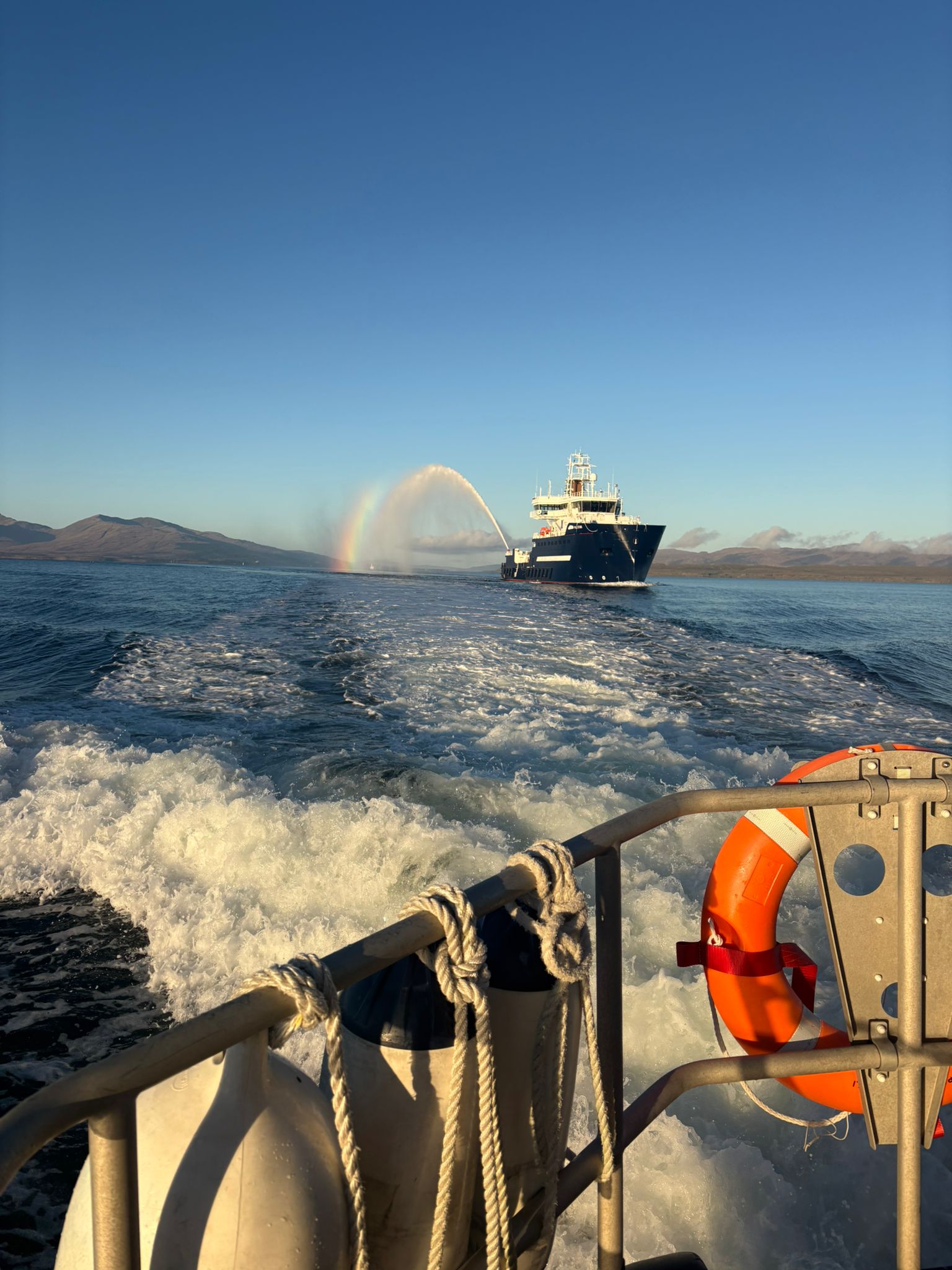 A photo taken over the stern of Oban's Shannon class lifeboat across calm seas to the new lighthouse tender vessel.