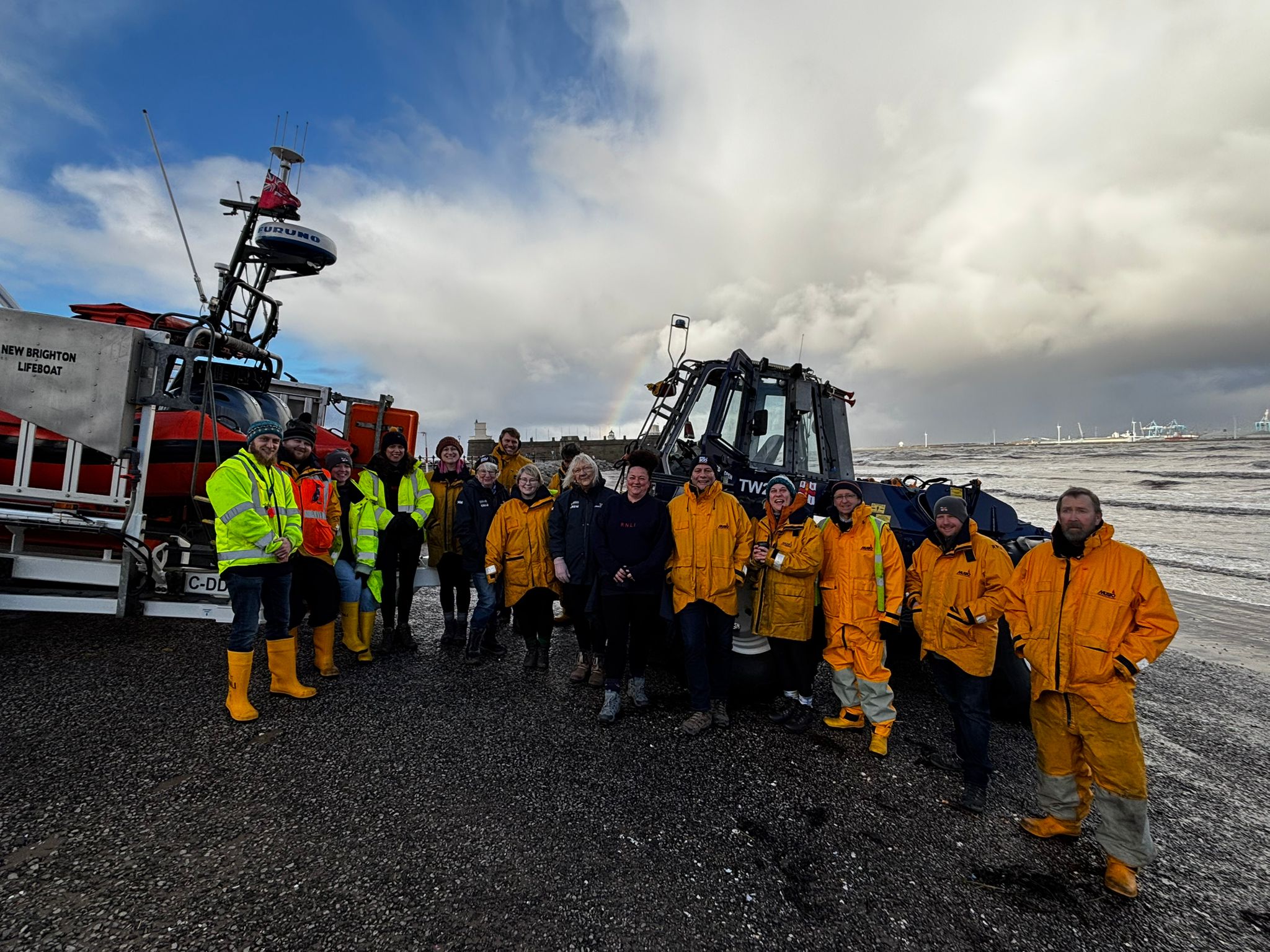 New Brighton RNLI volunteers pose for a group photo, in their yellows, in front of the tractor, lifeboat and carriage, on New Brighton beach.