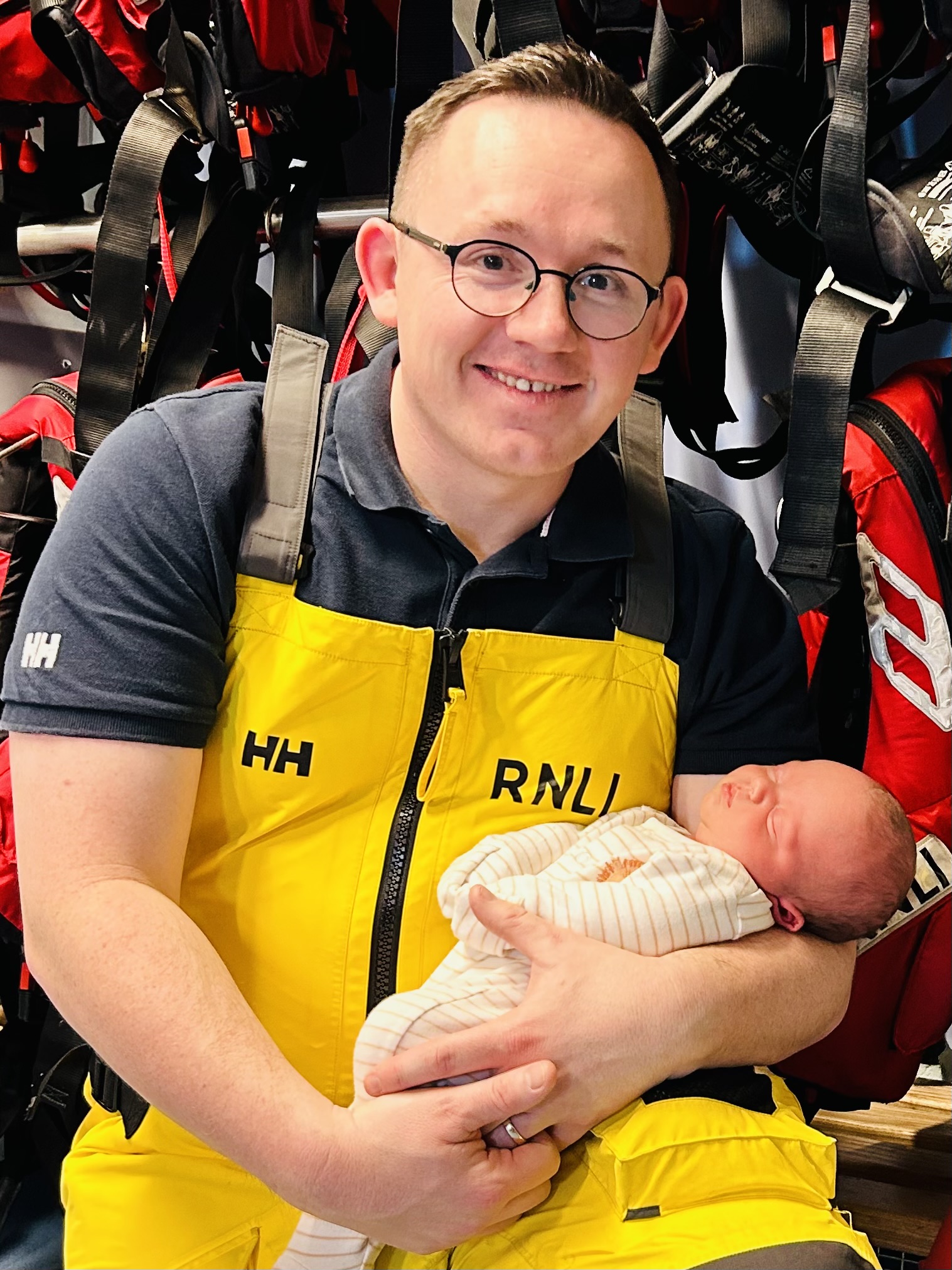 Photo of a smiling dad in RNLI yellow kit with his new baby 