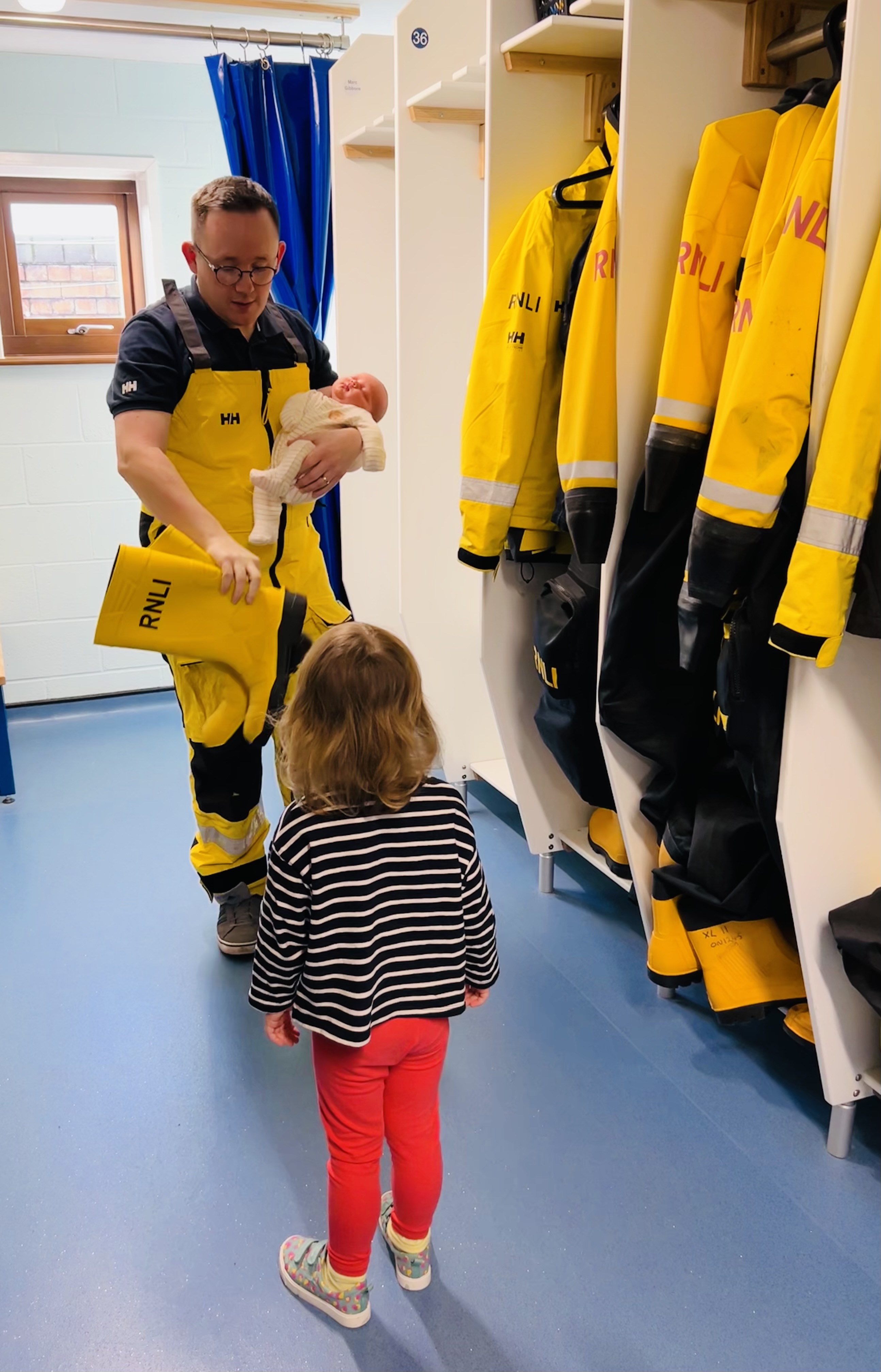Photo shows volunteer crew member Gerwyn in his RNLI yellows, showing his young daughter and baby son his yellow wellies