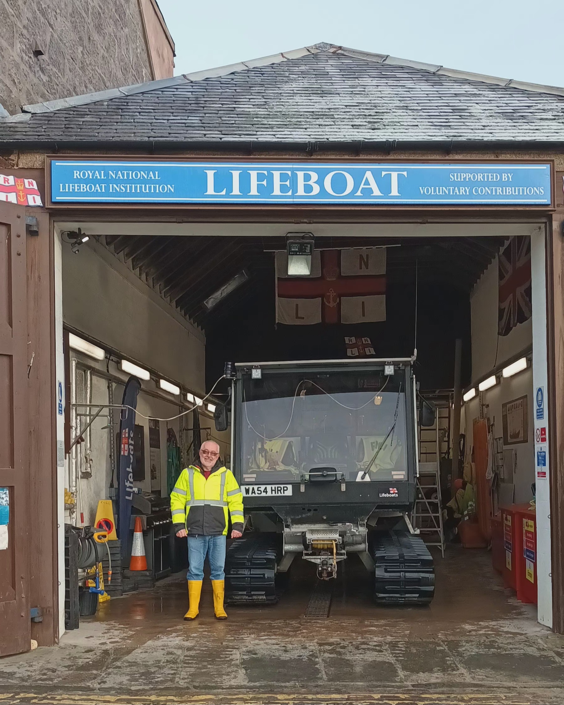 Peter Esson, new Lifeboat Operations Manager for Stonehaven RNLI stands at the entrance to the boat shed next to the tractor rig

