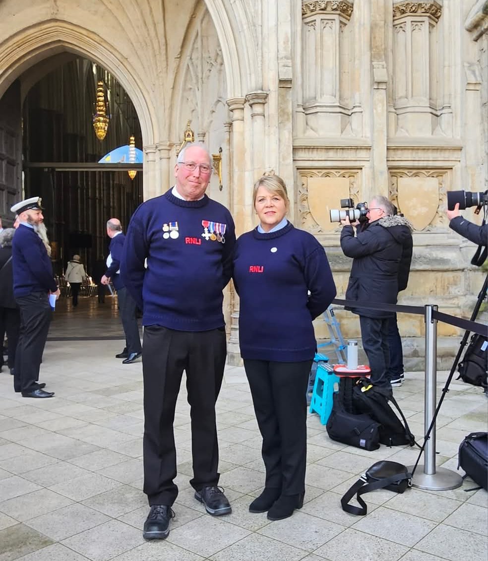 Newquay RNLI lifeboat press officer and newly qualified Launch Authority, Ann-Marie Dale attending a service of Thanksgiving at Westminster Abbey with the station's Lifeboat Operations Manager, Gareth Horner, to mark the charity's 200th anniversary on 4 March 2024. Both are dressed in their smart RNLI guernseys, stood in front of the abbey with lifeboat crew from other stations in the background.