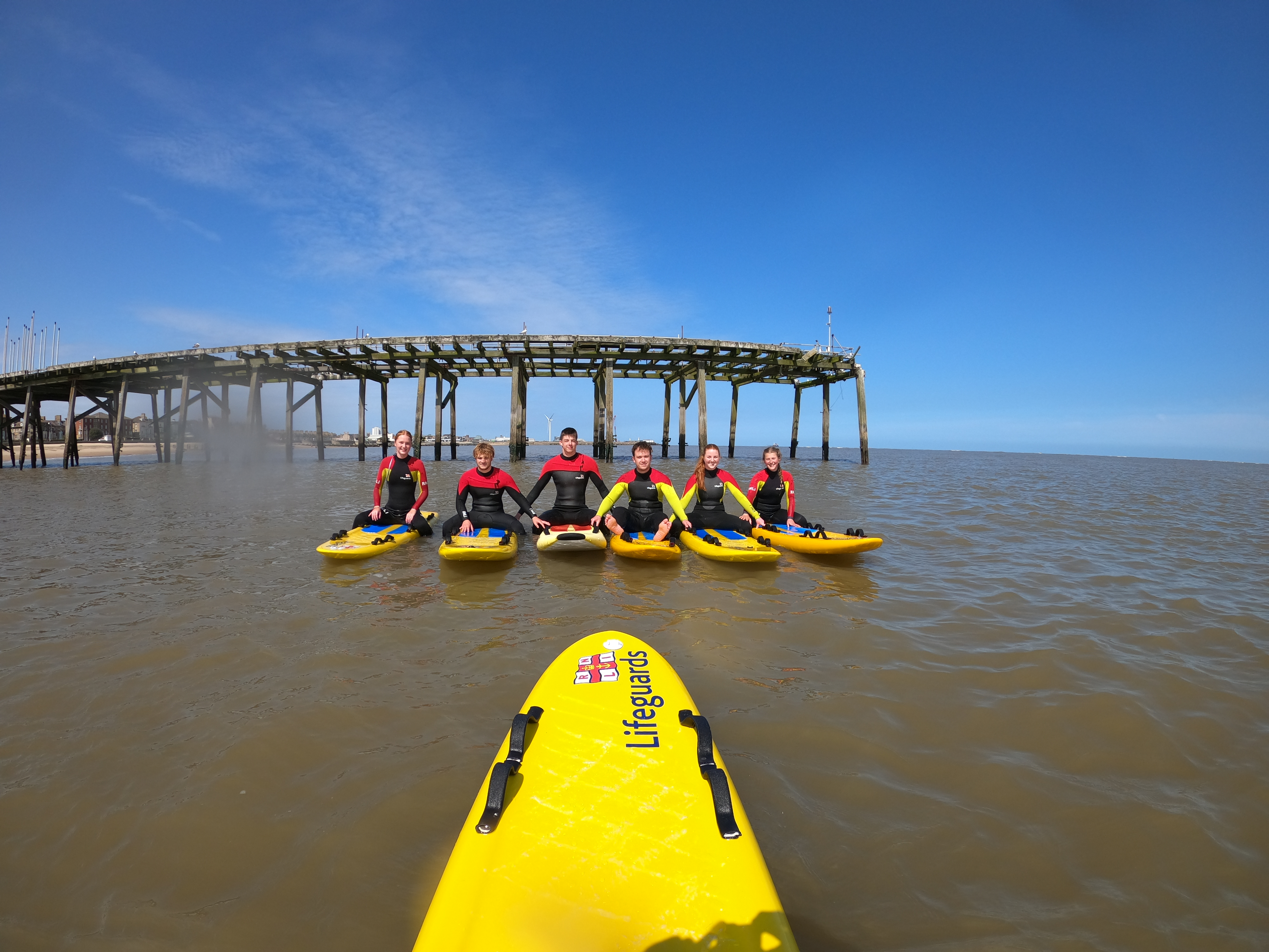 RNLI Lifeguards on rescue boards in line in water with pier in the background. Lifeguards in full kit