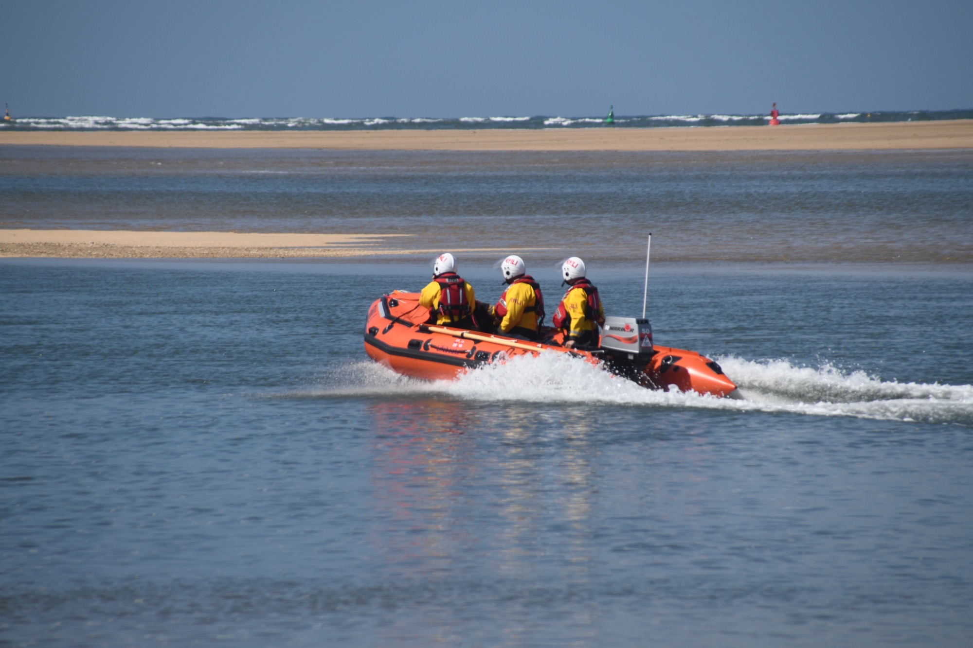 Inshore lifeboat Peter Wilcox launched to three people cut off by incoming tide Three volunteer crew in full inshore lifeboat kit in inshore lifeboat on open water. Sandbank in the background
