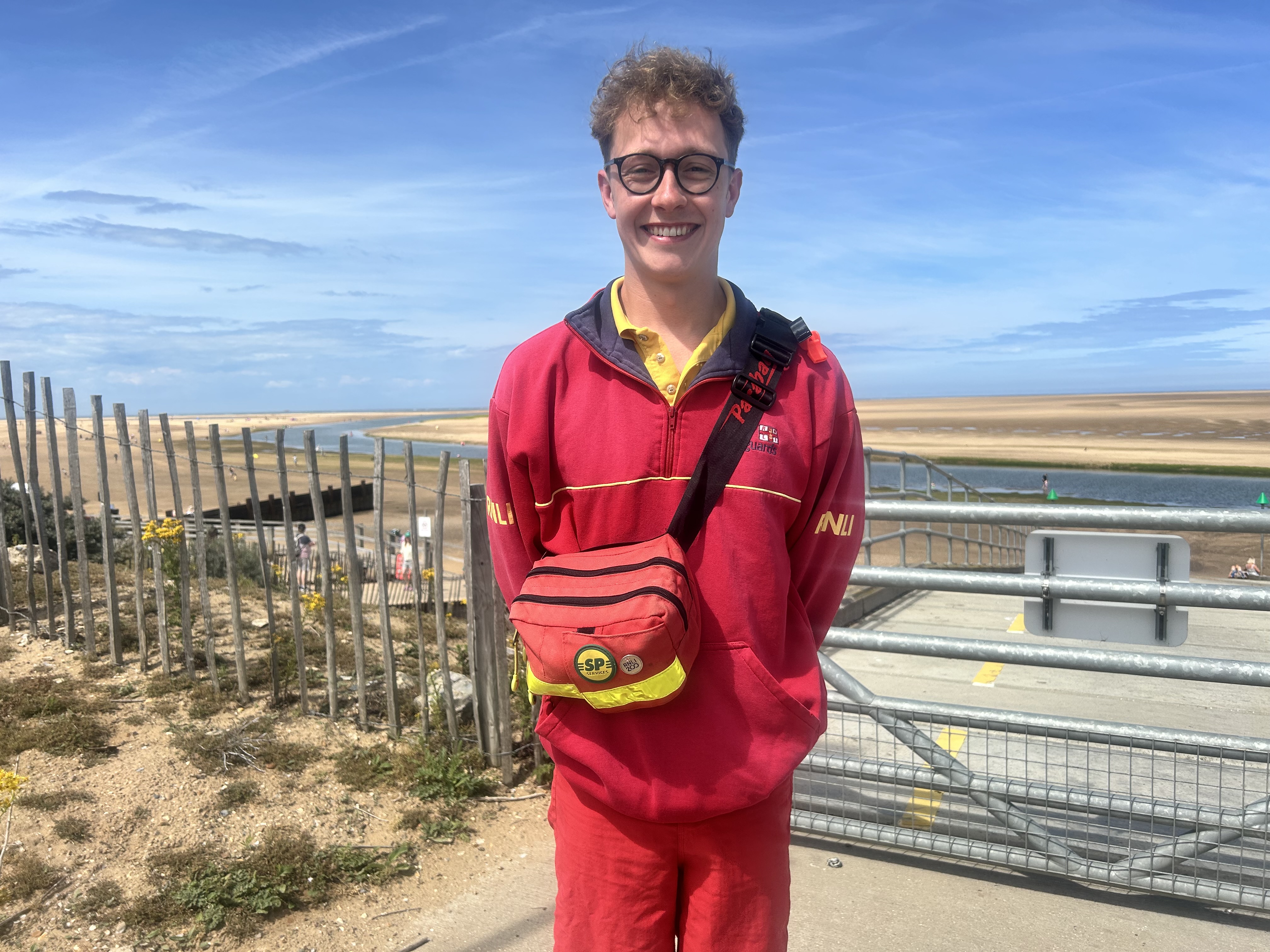 RNLI Lifeguard in full RNLI lifeguard kit with beach in background 