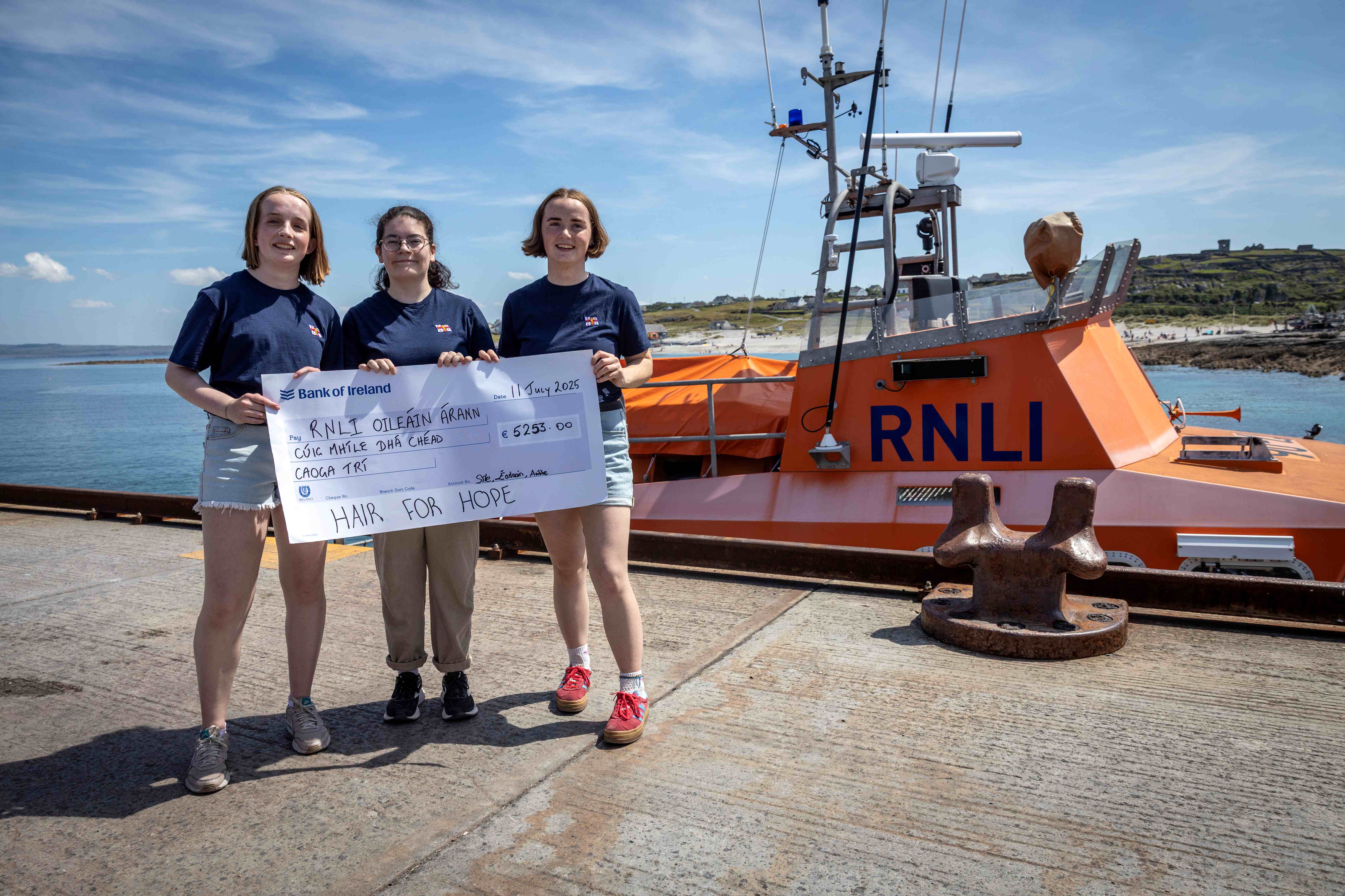 Sile, Aoibhe and Éadaoin holding a cheque in front of the Aran Islands lifeboat
