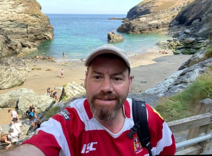 Simon Wiggins by the sea in red and white striped top. Sea and cliffs in the background