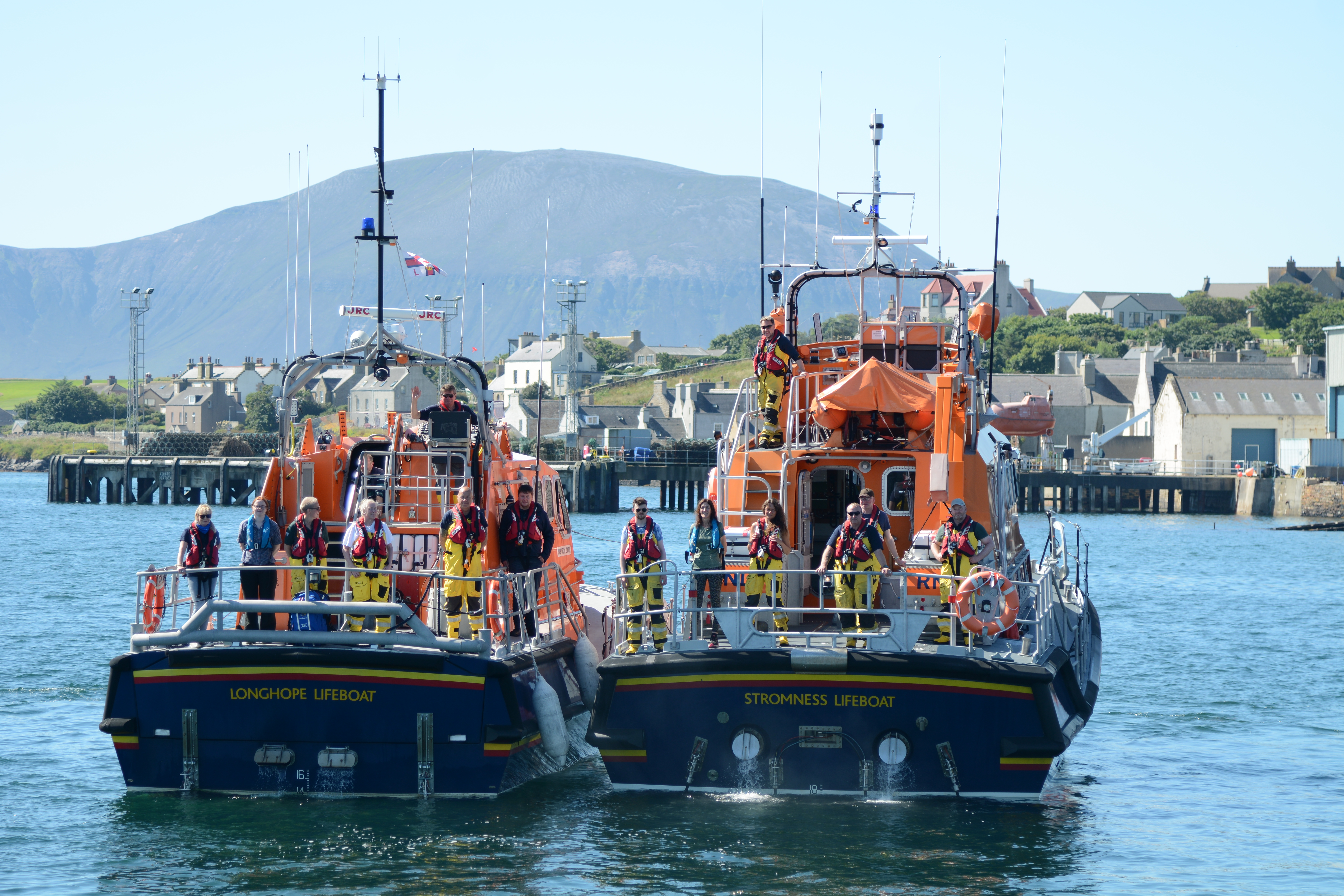 Crews of two lifeboats, viewed from the stern, line up to pose for a photo