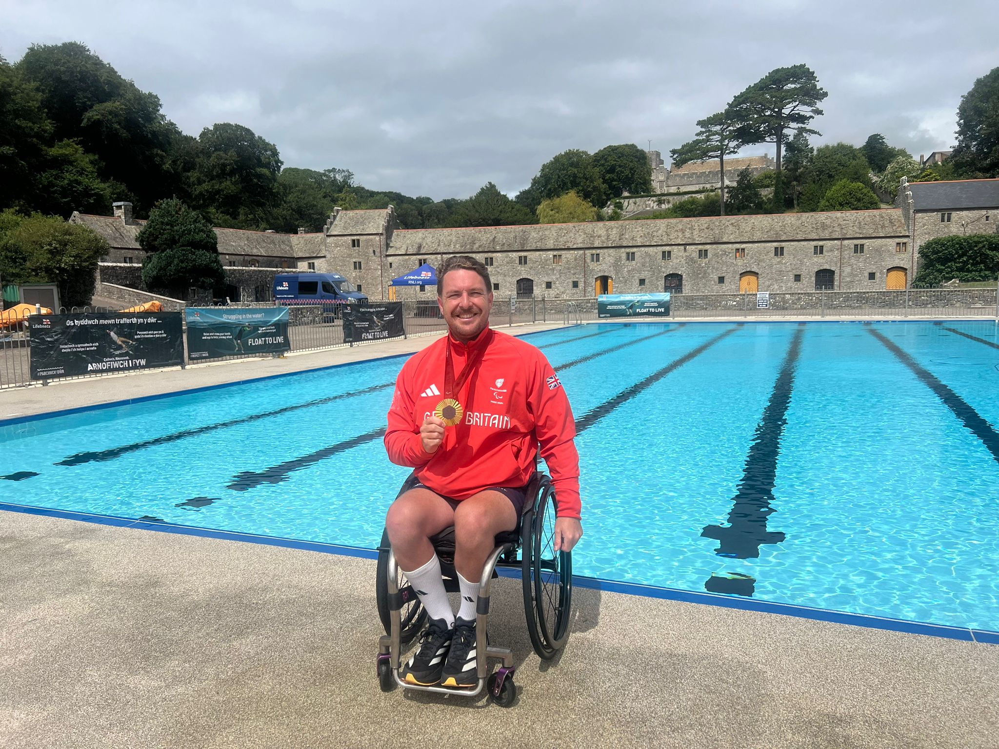 Ben Pritchard in wheelchair holding gold Paralympic medal smiling to camera