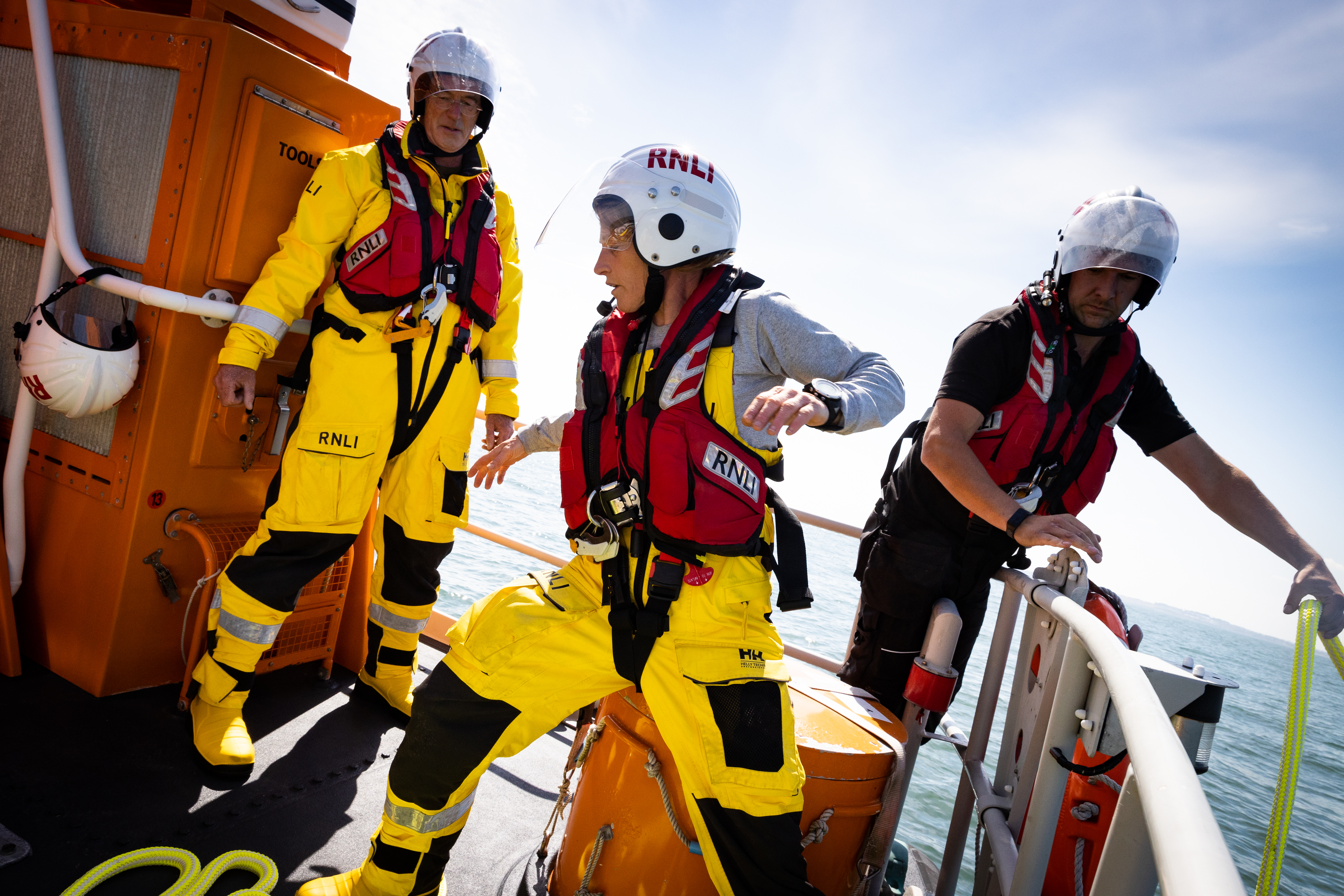 Three volunteer crew members of Howth RNLI are pictured moving on the deck of the All-Weather Lifeboat. Two other crew are visible in the background. All three are conducting a towing exercise.
