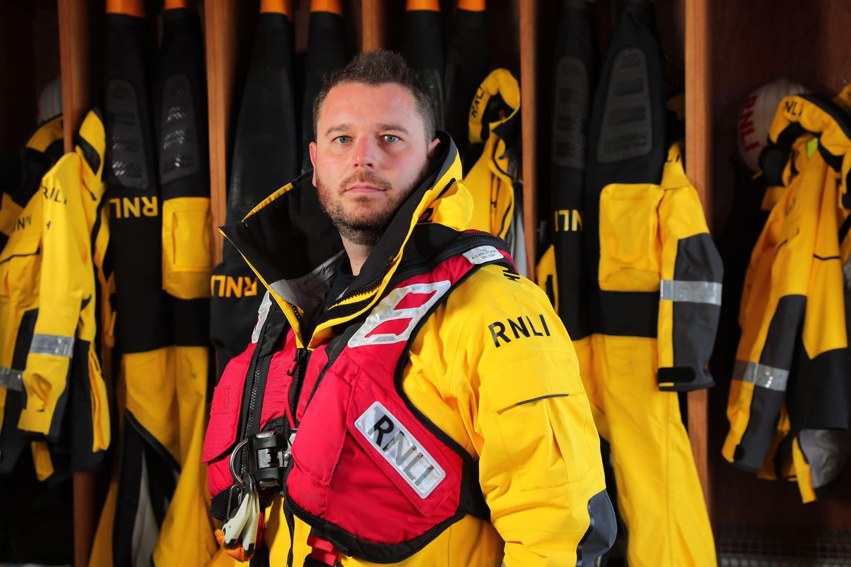 Ian Martin, crew member at Howth RNLI is standing in the boathouse in full crew kit.