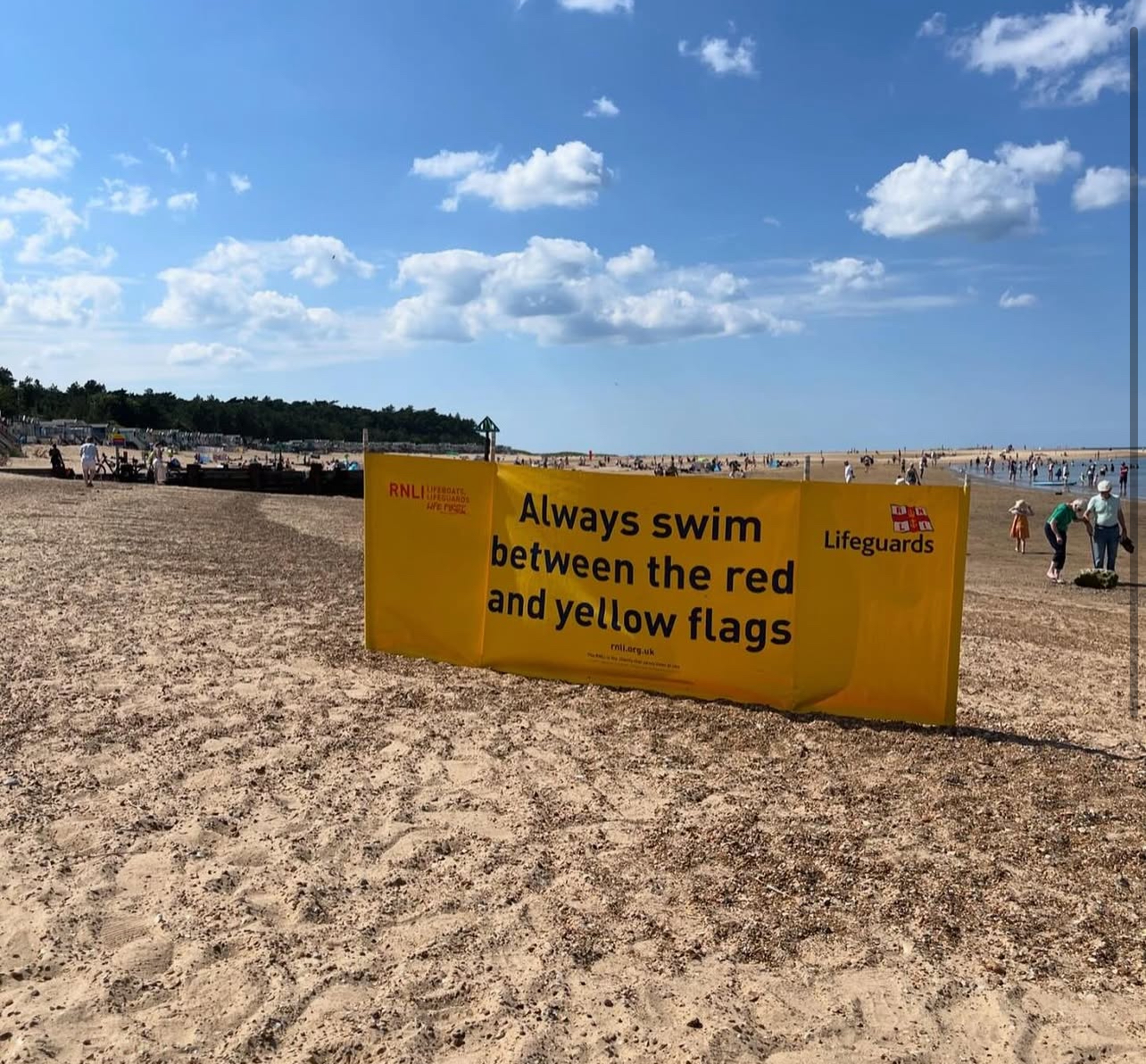 Always swim between the red and yellow flags sign on the beach. Sand and people in the background
