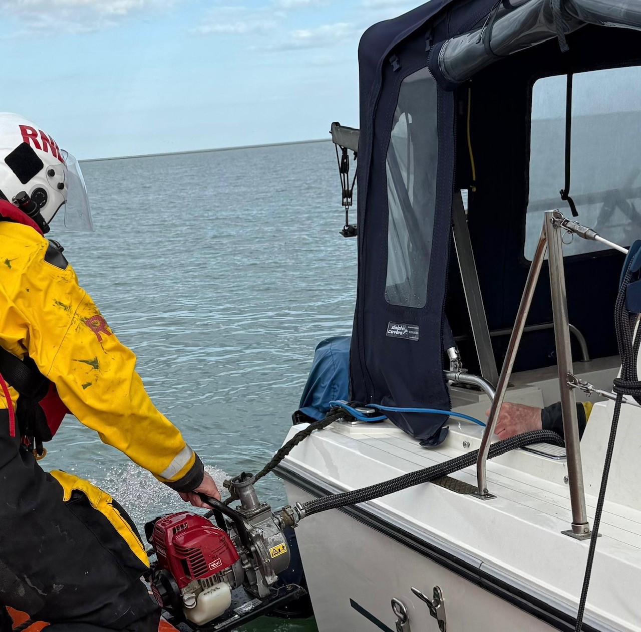 Lifeboat moored next to the casualty vessel using a mechanical pump to remove water from rear compartment
