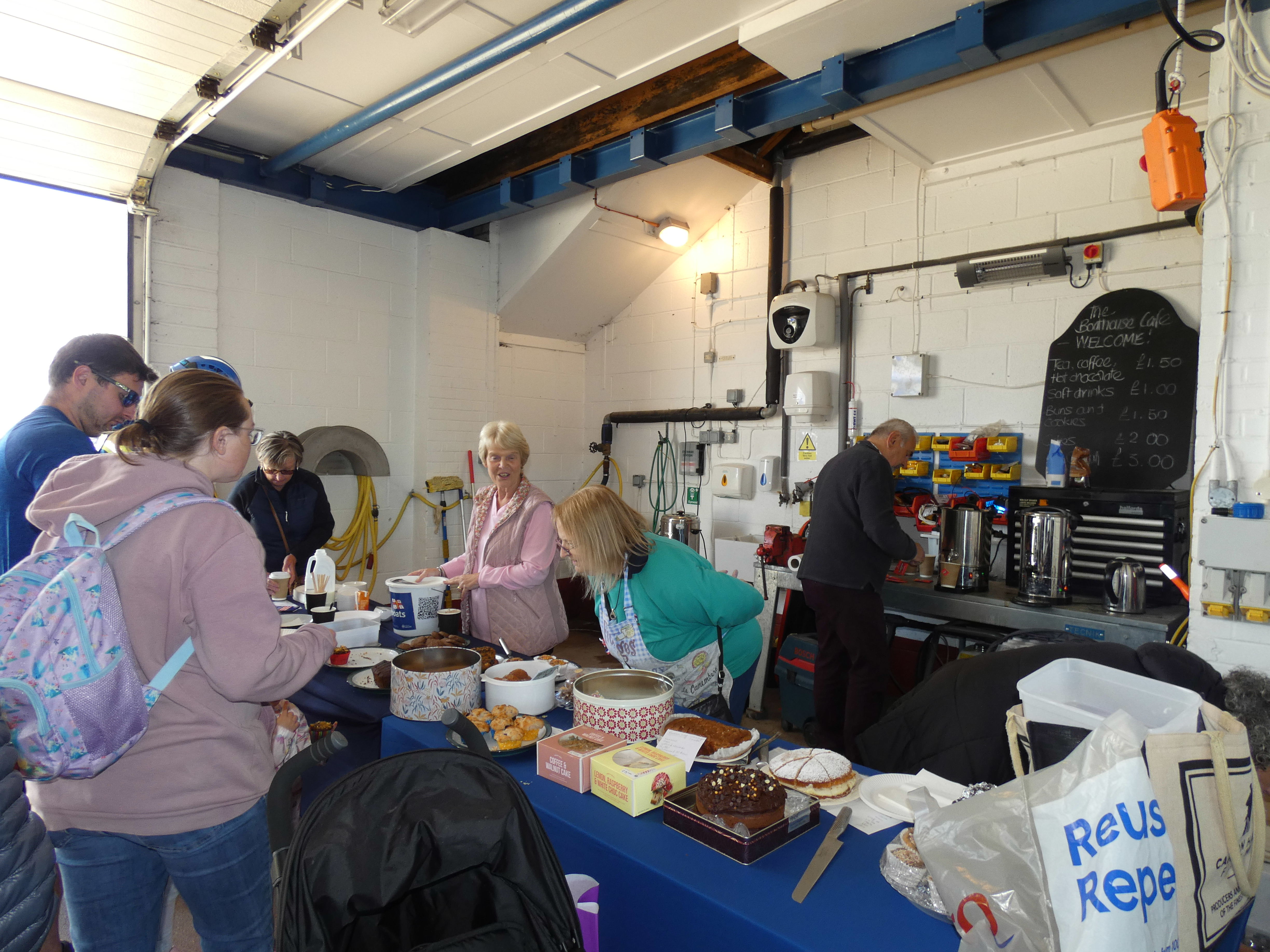 people buyong cakes and biscuits at a table in the boathouse