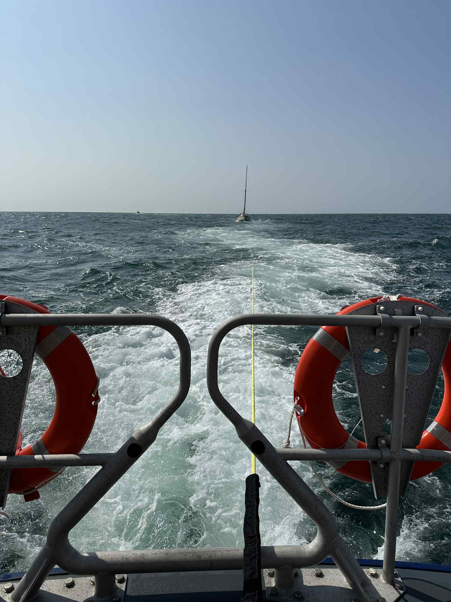 Yacht Feeling fantastic under tow by Wells RNLI breaking water behind the lifeboat and yacht in distance blue skies