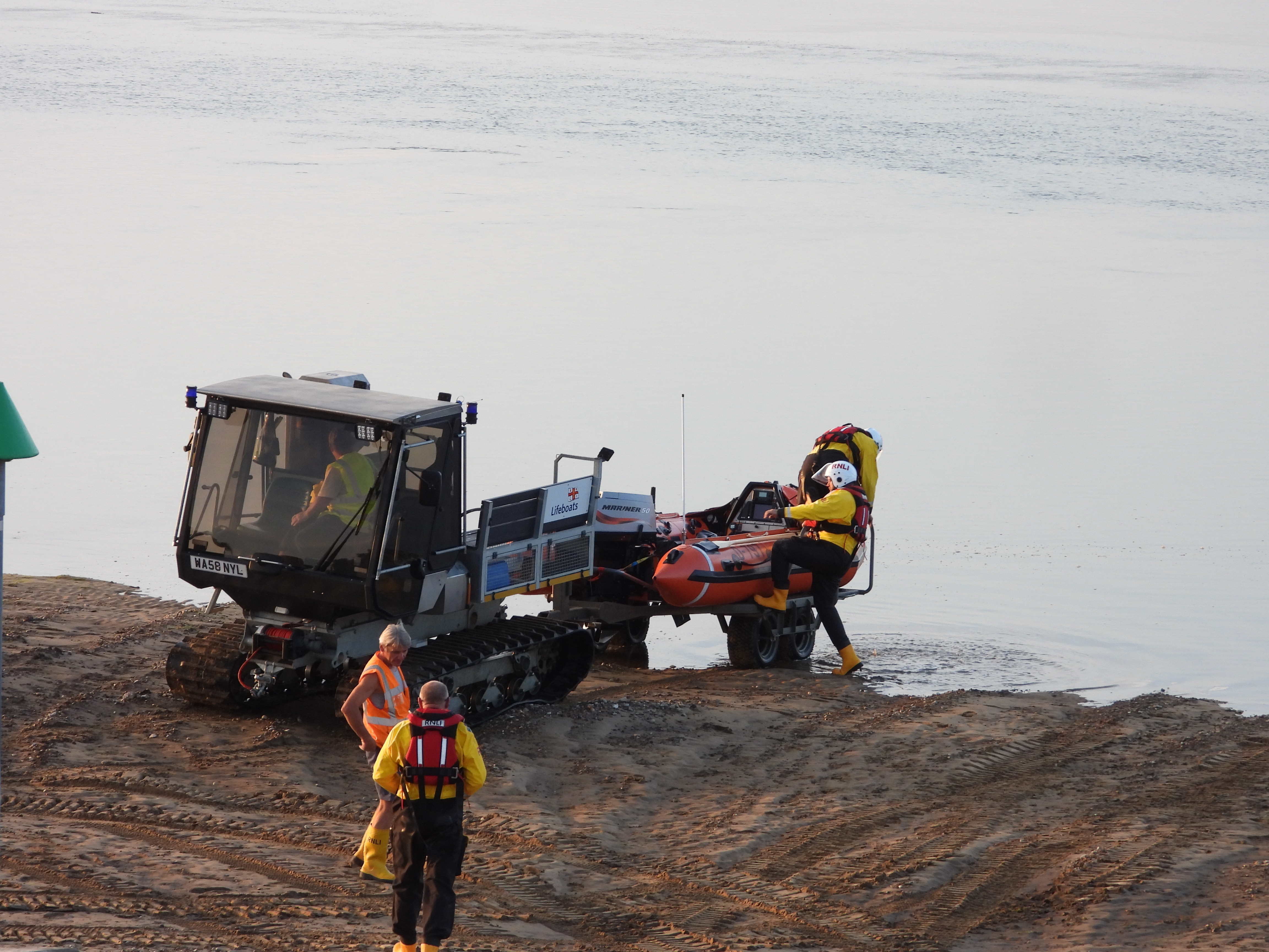 Wells RNLI D class lifeboat and launching and recovery vehicle launching inshore lifeboat in water at sunset with a crew of three