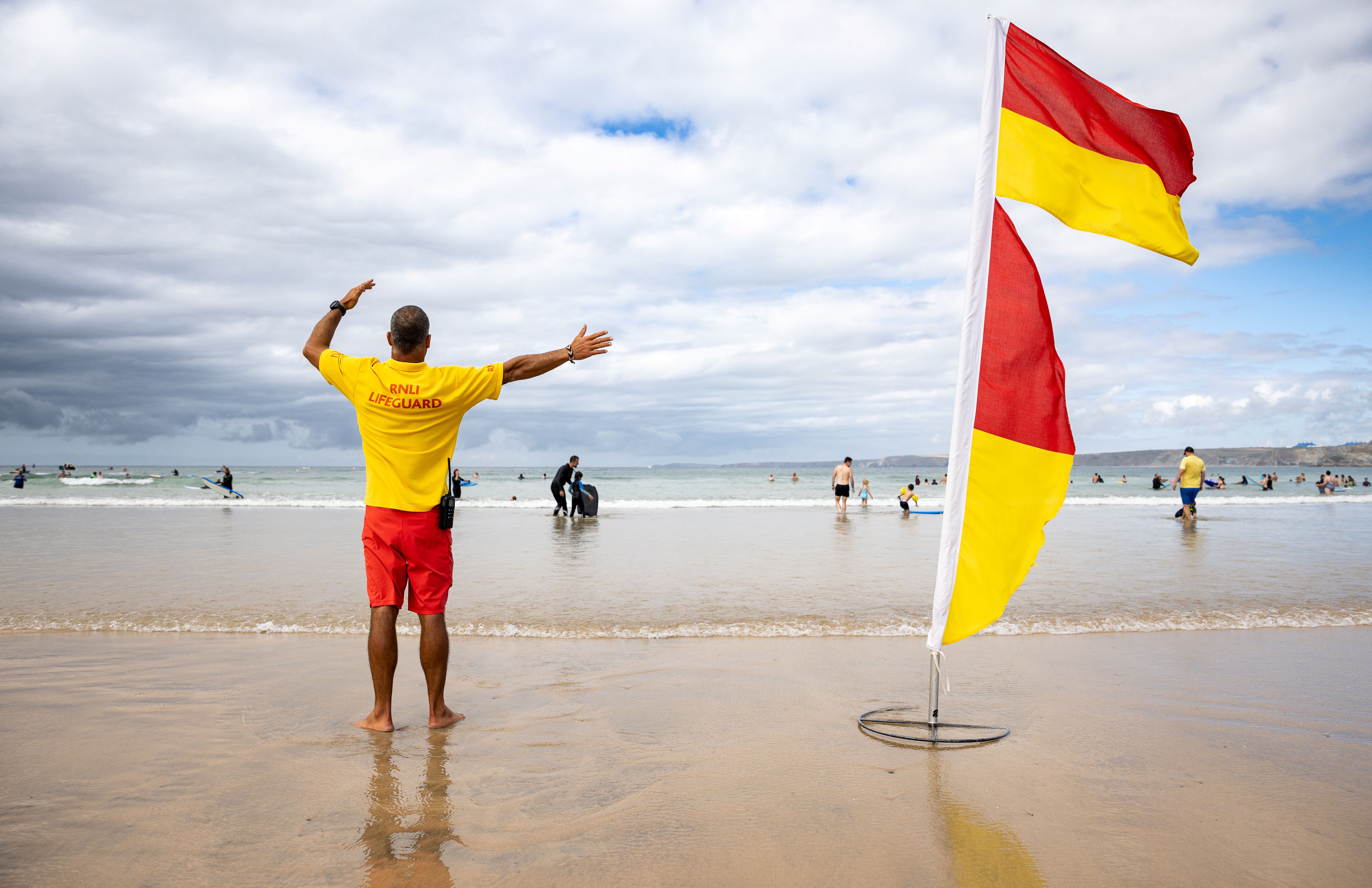 RNLI lifeguard on duty stood on a beach next to a red and yellow flag