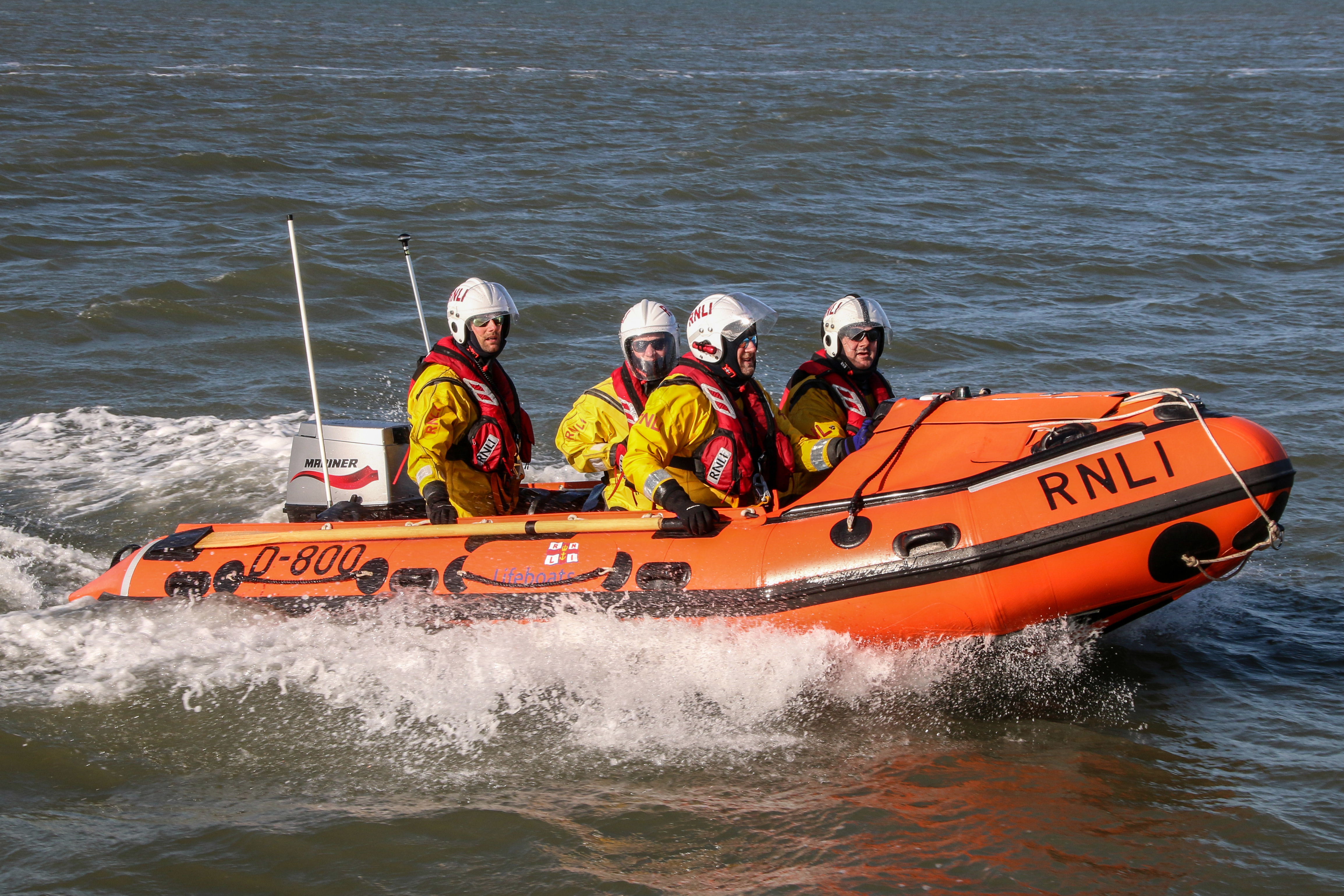 An inshore lifeboat travels at speed with four crew on board