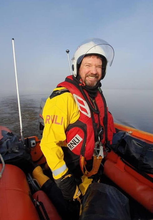 A lifeboat helm kneels at the tiller of an inshore lifeboat