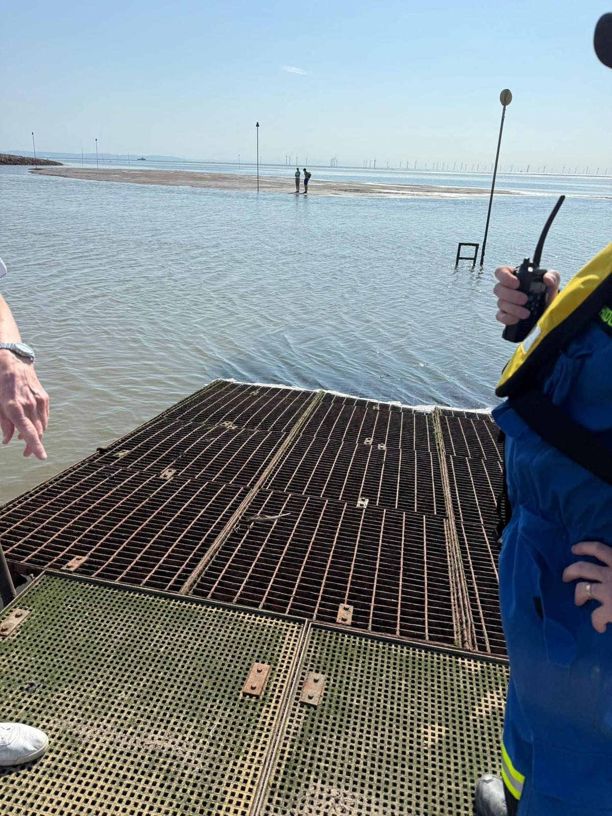 Taken from a pontoon edge, with pontoon visible at bottom of frame, two casualties can be seen across the river Alt, standing on a shrinking sandbank, waiting to be rescued.