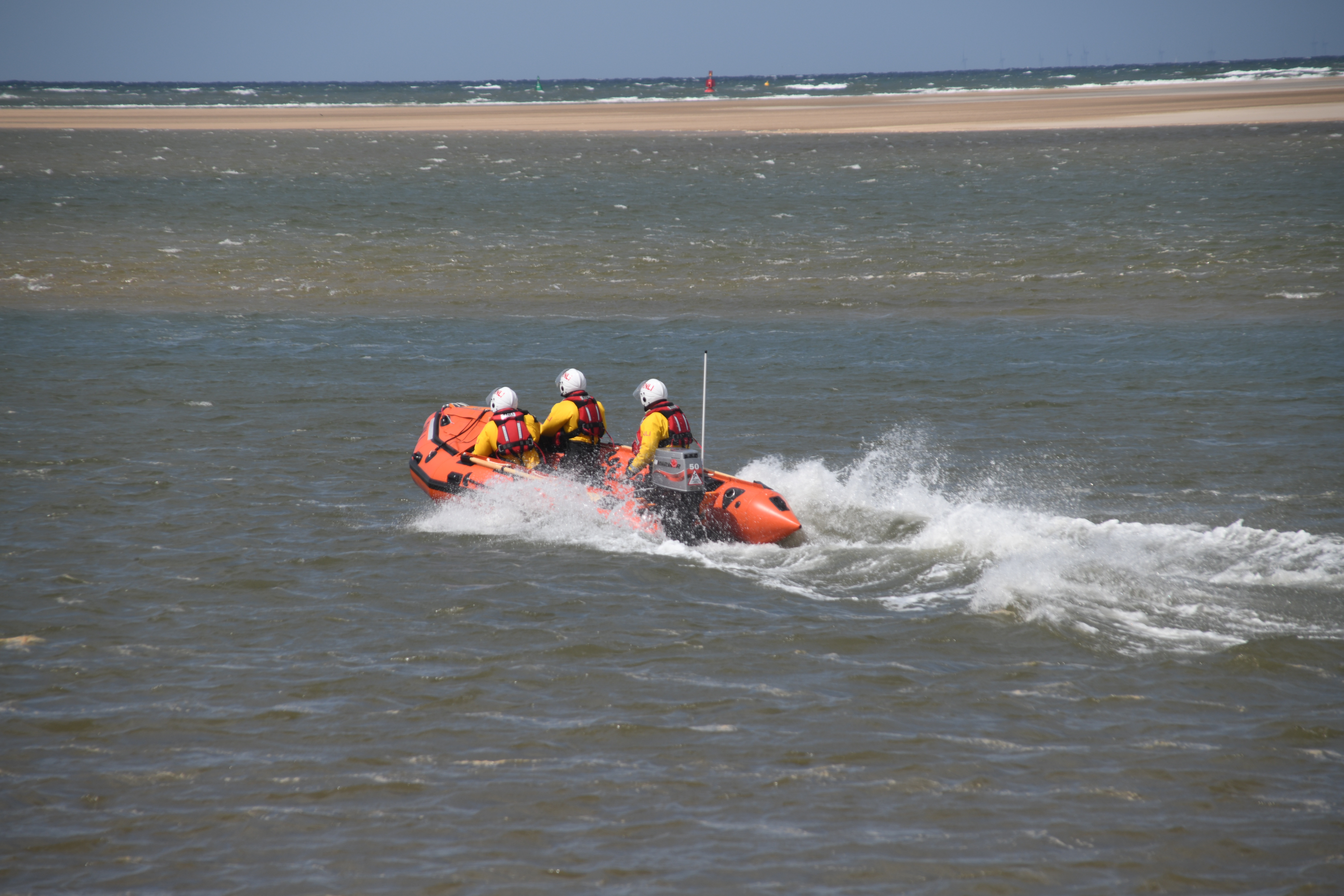 Inshore lifeboat Peter Wilcox heading to casualties cut off by incoming tide Three RNLI volunteers on inshore lifeboat in full inshore lifeboat kit.
