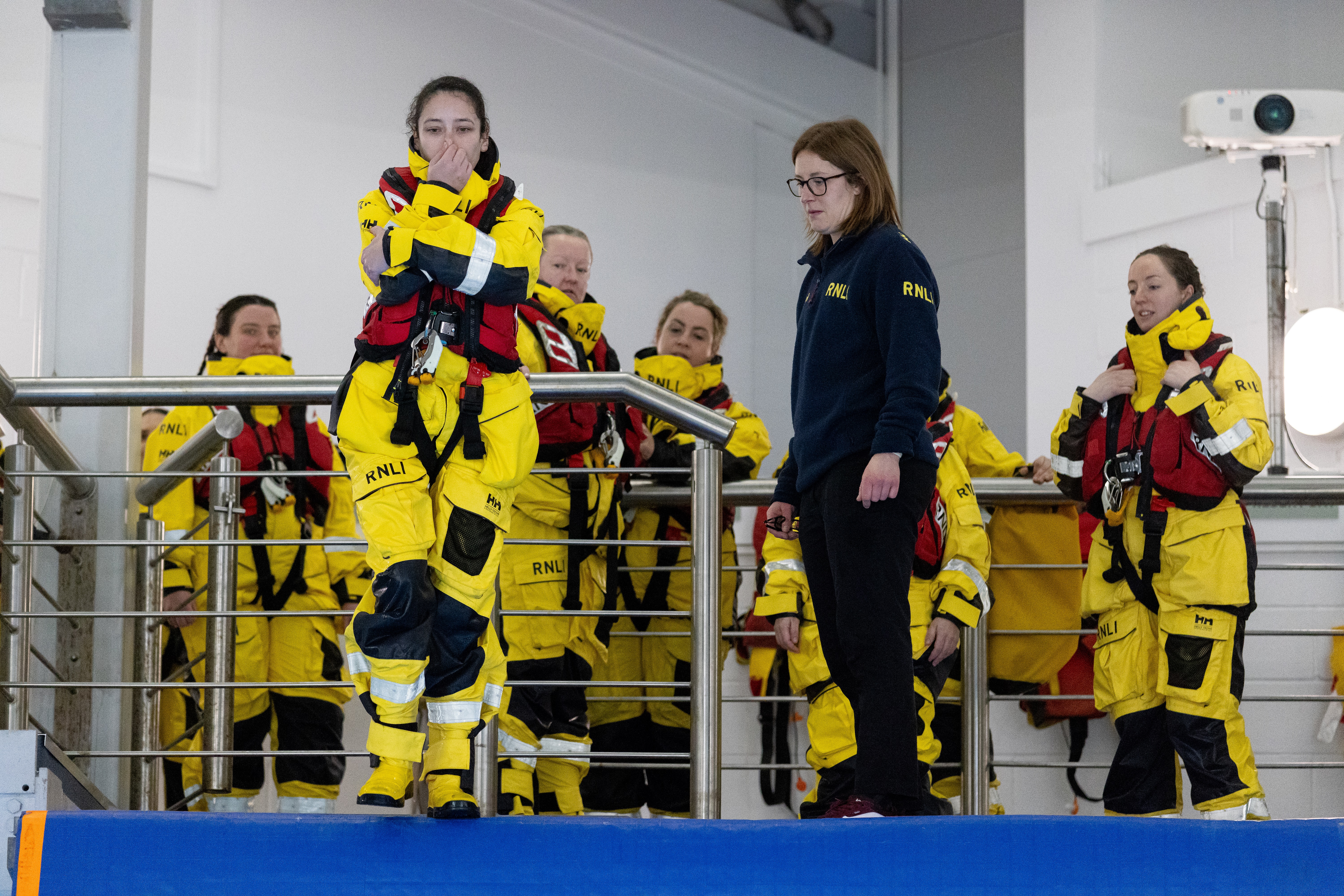 Woman in full yellow lifeboat kit and lifejacket holds her nose before jumping into the Sea Survival Pool.
