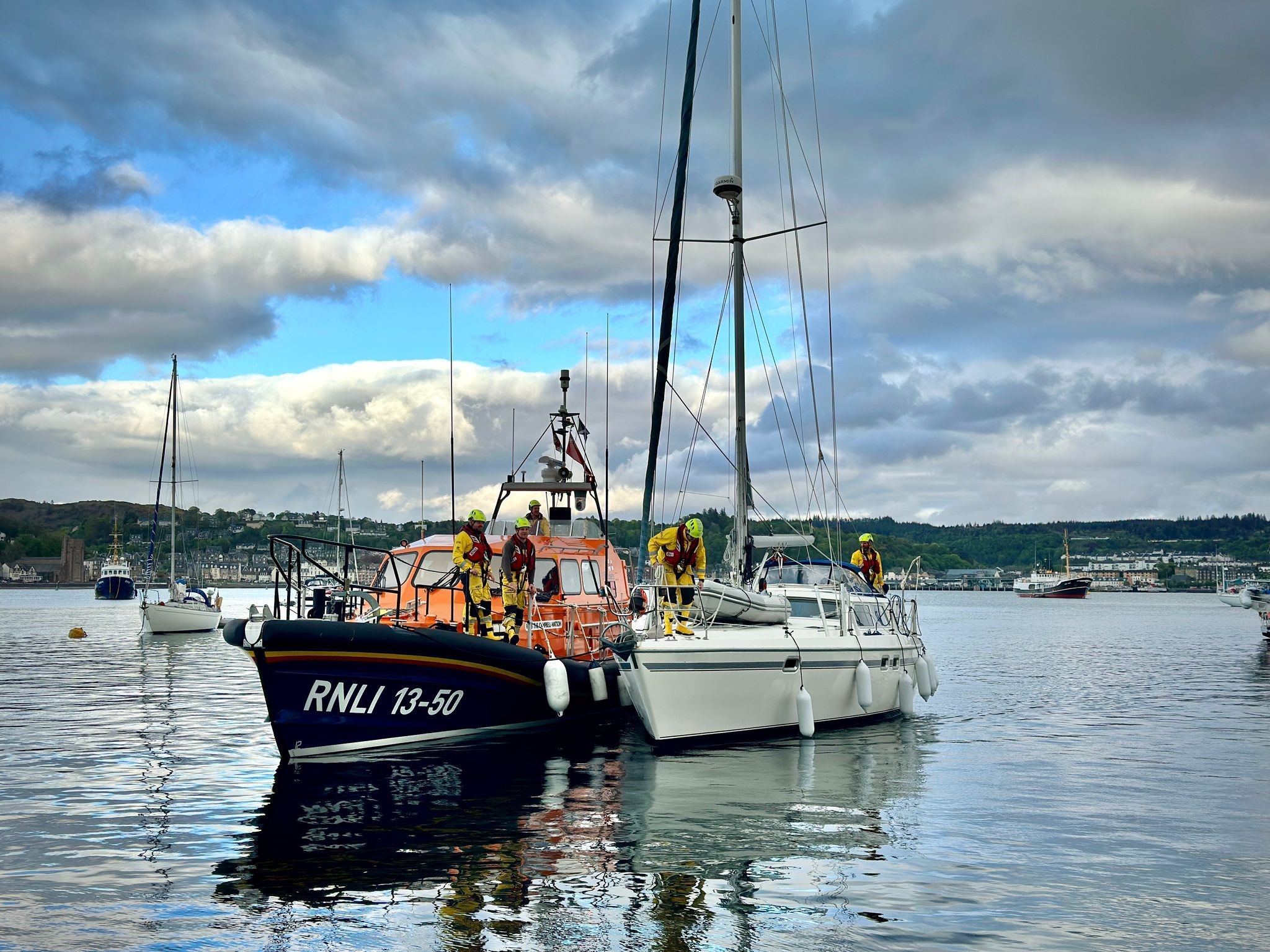 A white yacht with the Shannon class lifeboat in a calm reflecting sea with Oban in the background
