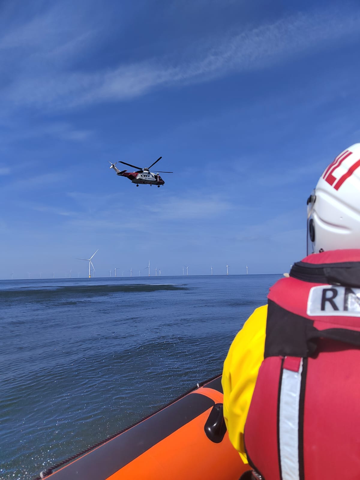 Photo from on board the Atlantic-85 lifeboat. A crew member can be seen from behind, and beyond them in the blue sky is Coastguard helicopter unit Rescue 936.