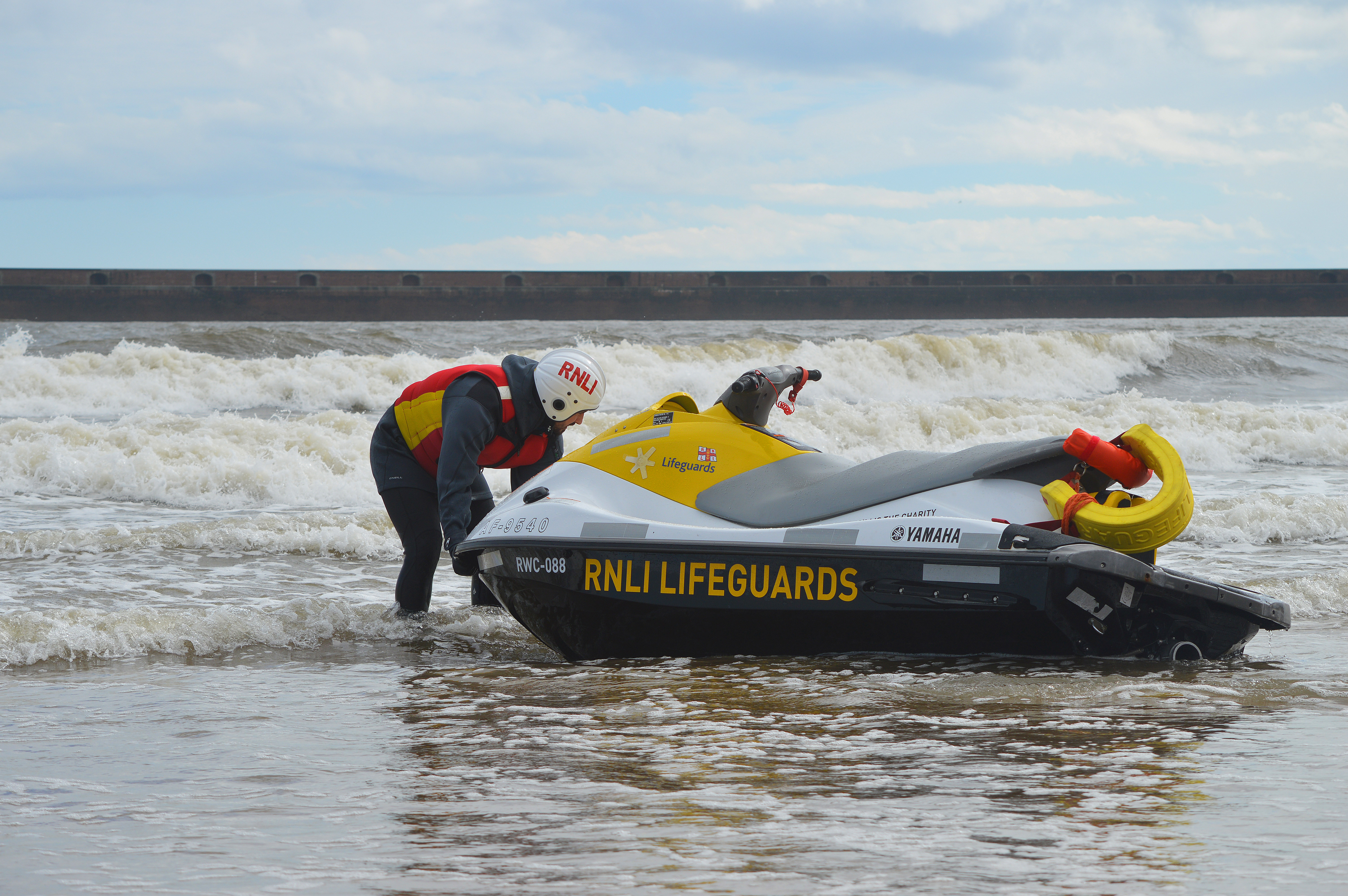 Lifeguard Supervisor Training with jet-ski at Roker Sunderland. liefguard in full RNLI lifeguard kit with RNLI jet ski on shore in the Surf. Sea and breaking waves in background
