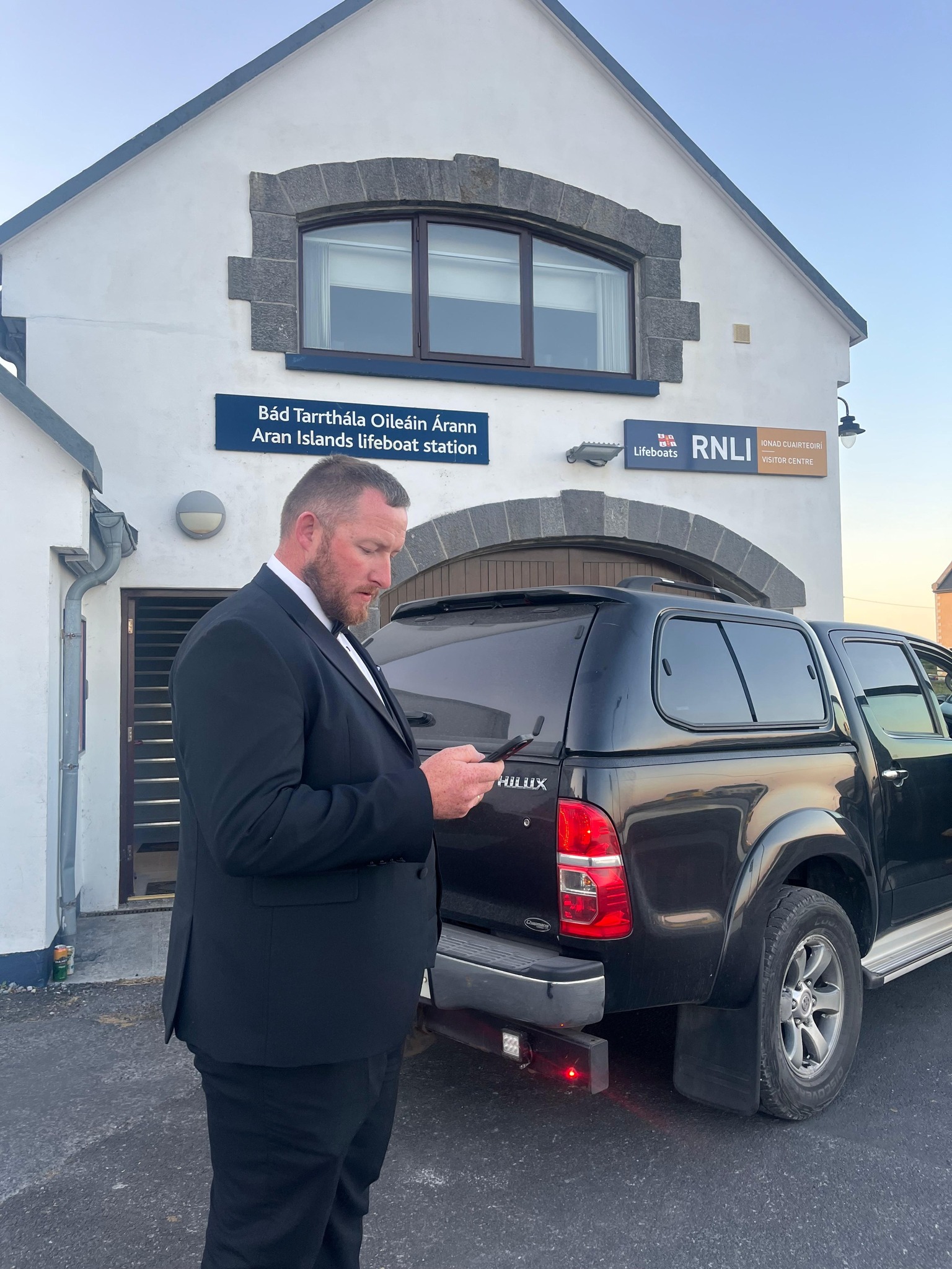 RNLI Coxswain Aonghus O hIarnain standing in front of the lifeboat station in his tux