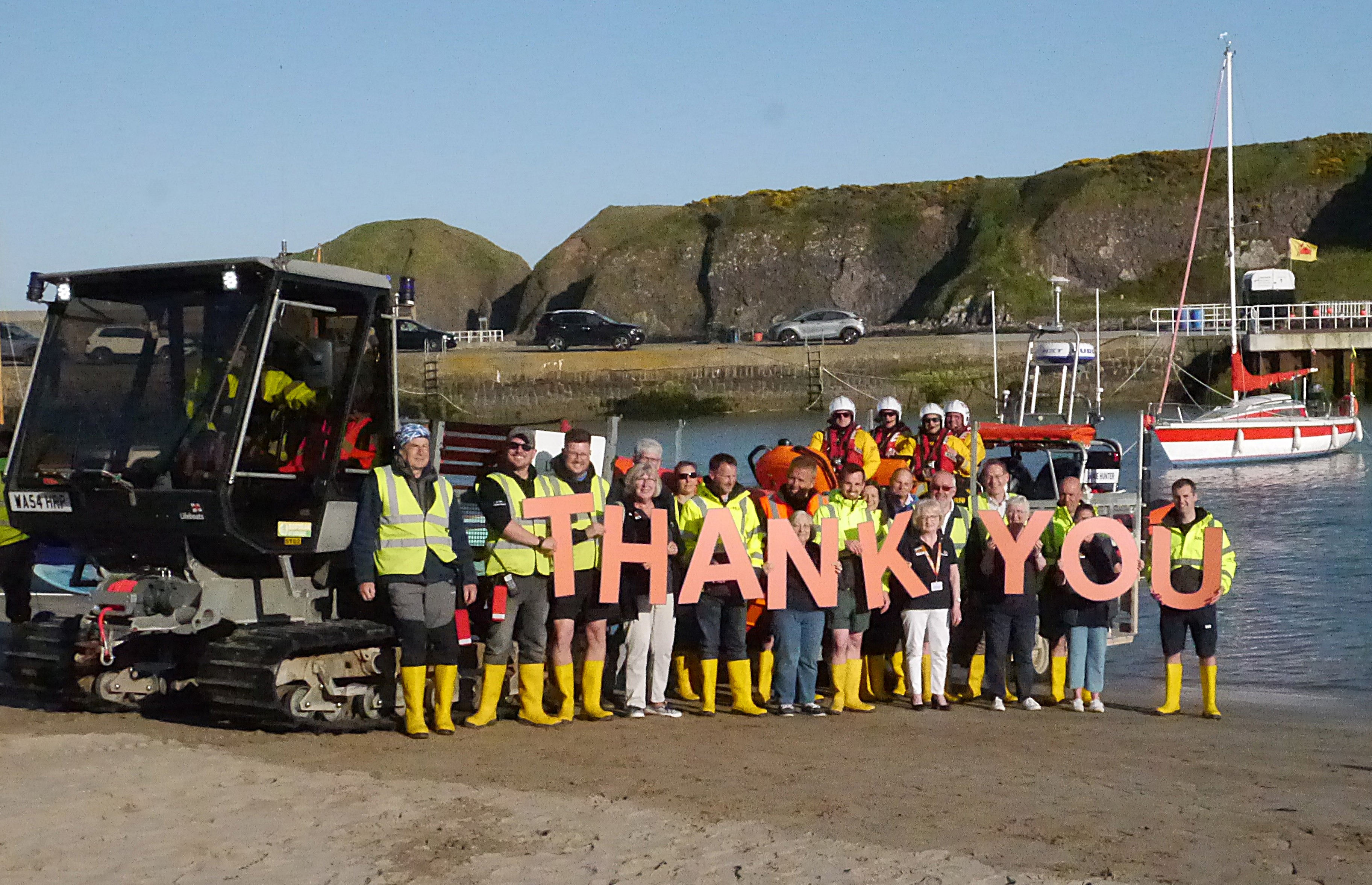 Volunteer crew holding large letters spelling out thank you, stood in front of the lifeboat and tractor at the harbour beach