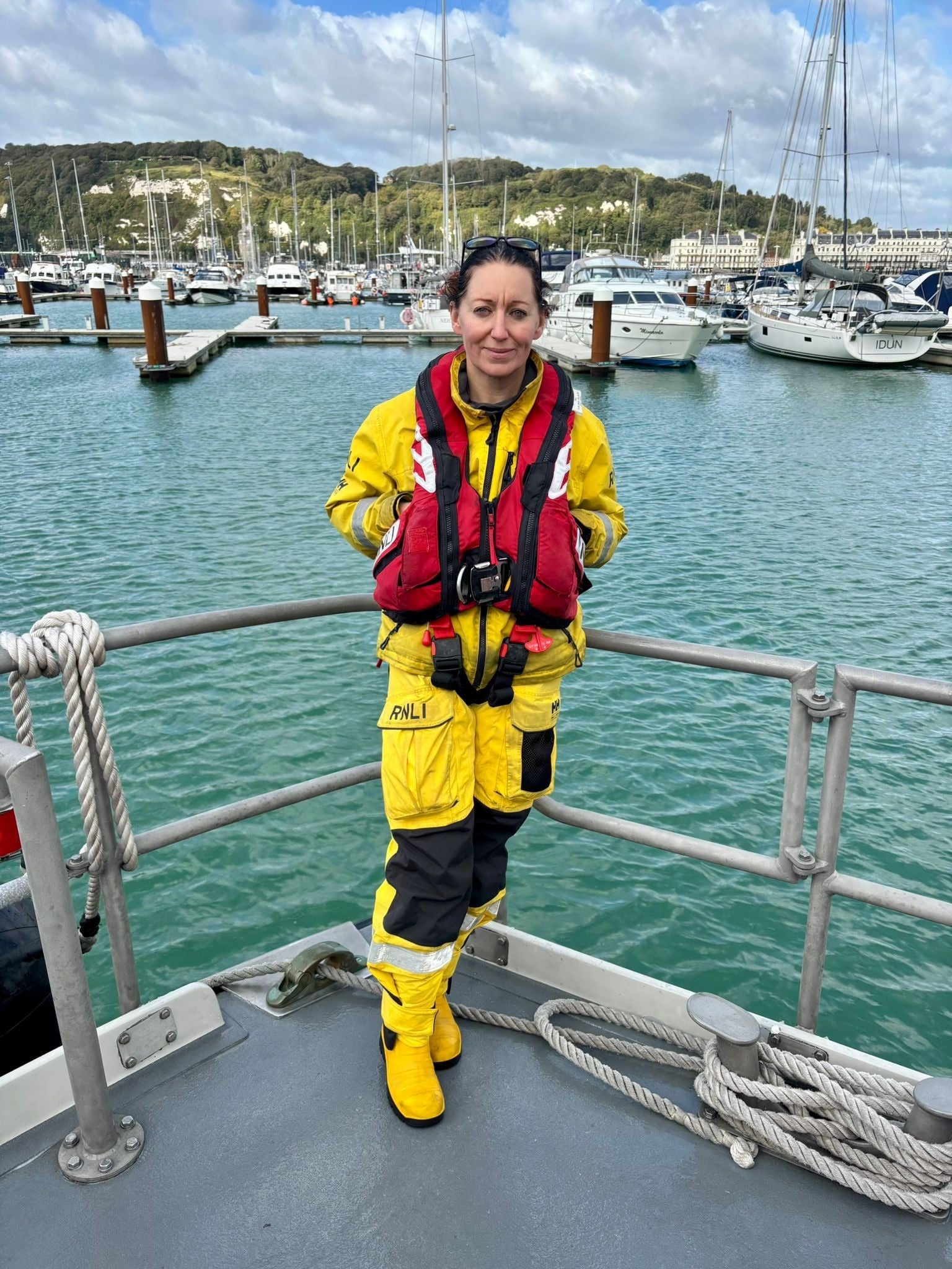 Woman in RNLI uniform stands on jetty overlooking the sea