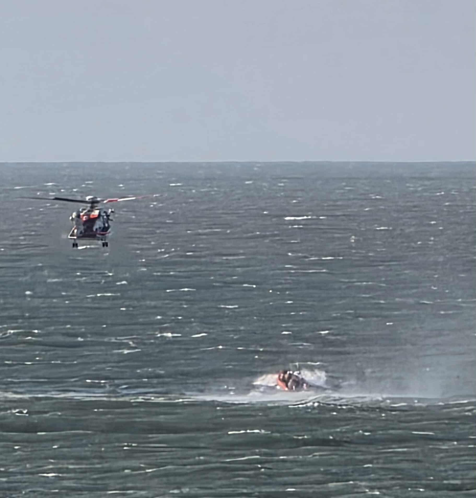 Helicopter above lifeboat in distance.