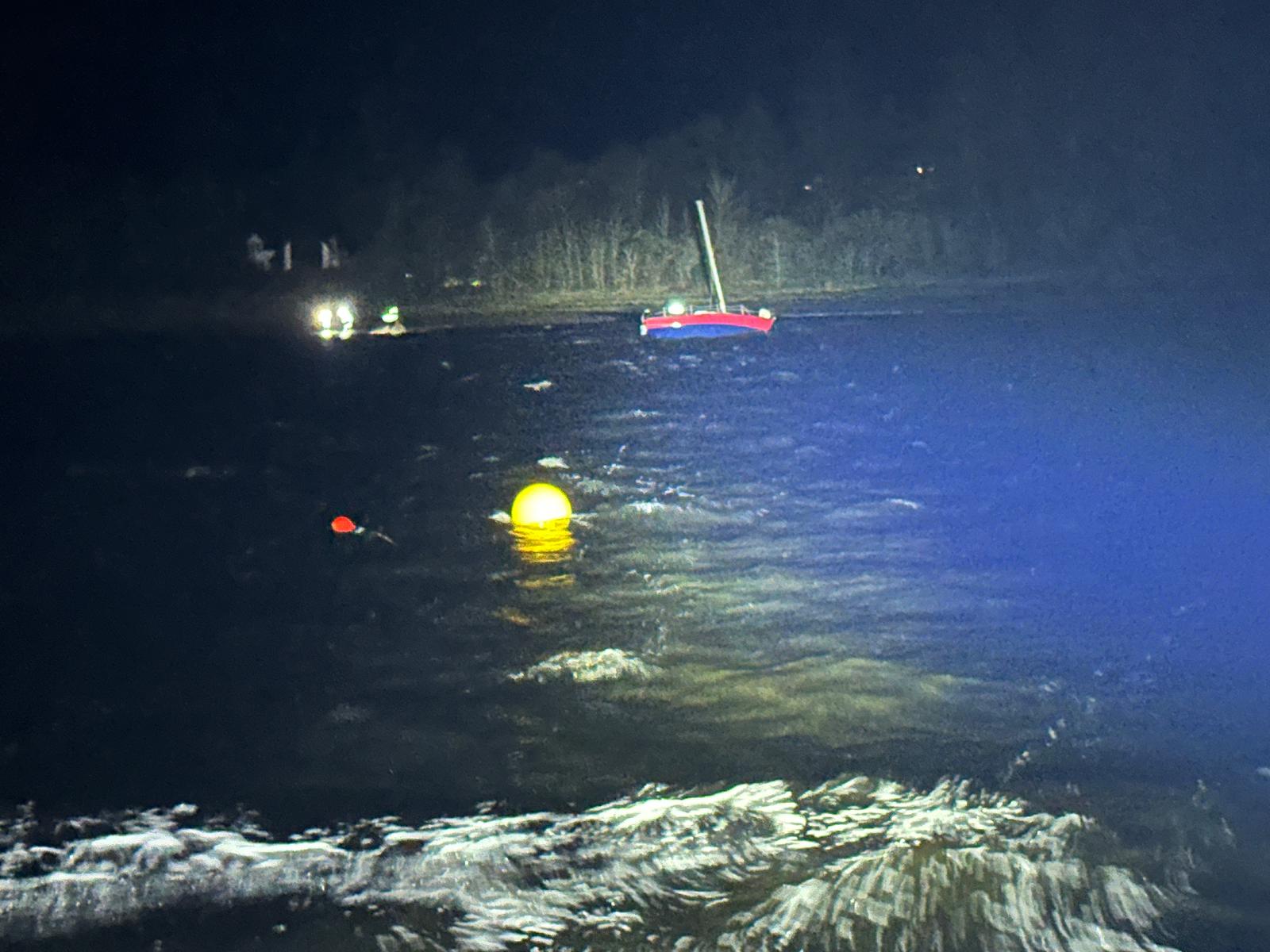 A nighttime photo of a red hulled yacht on its side close to the shore with teh scene illuminated by the lifeboat's searchlight
