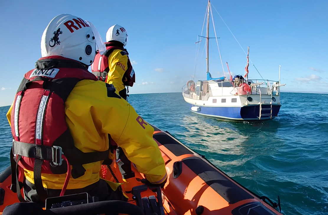 Two crew in yellow suits approach the blue and white yacht