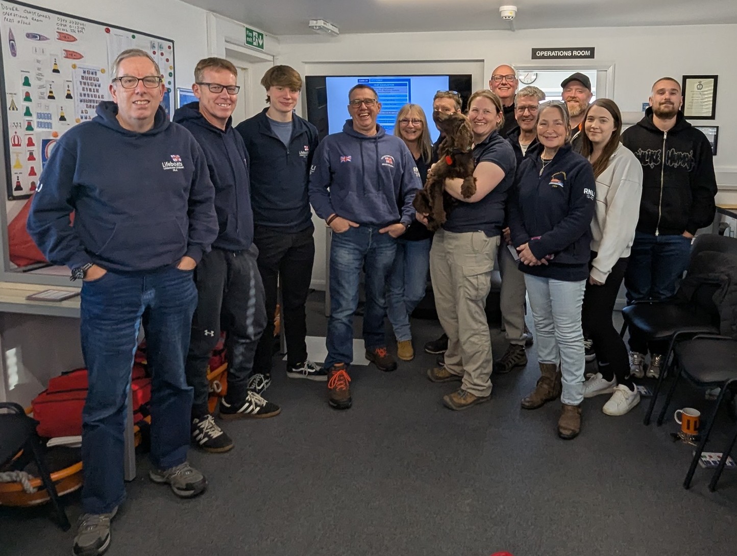 A group of RNLI volunteers standing in a half circle with their trainer Rosie Allen who is holding her spaniel dog