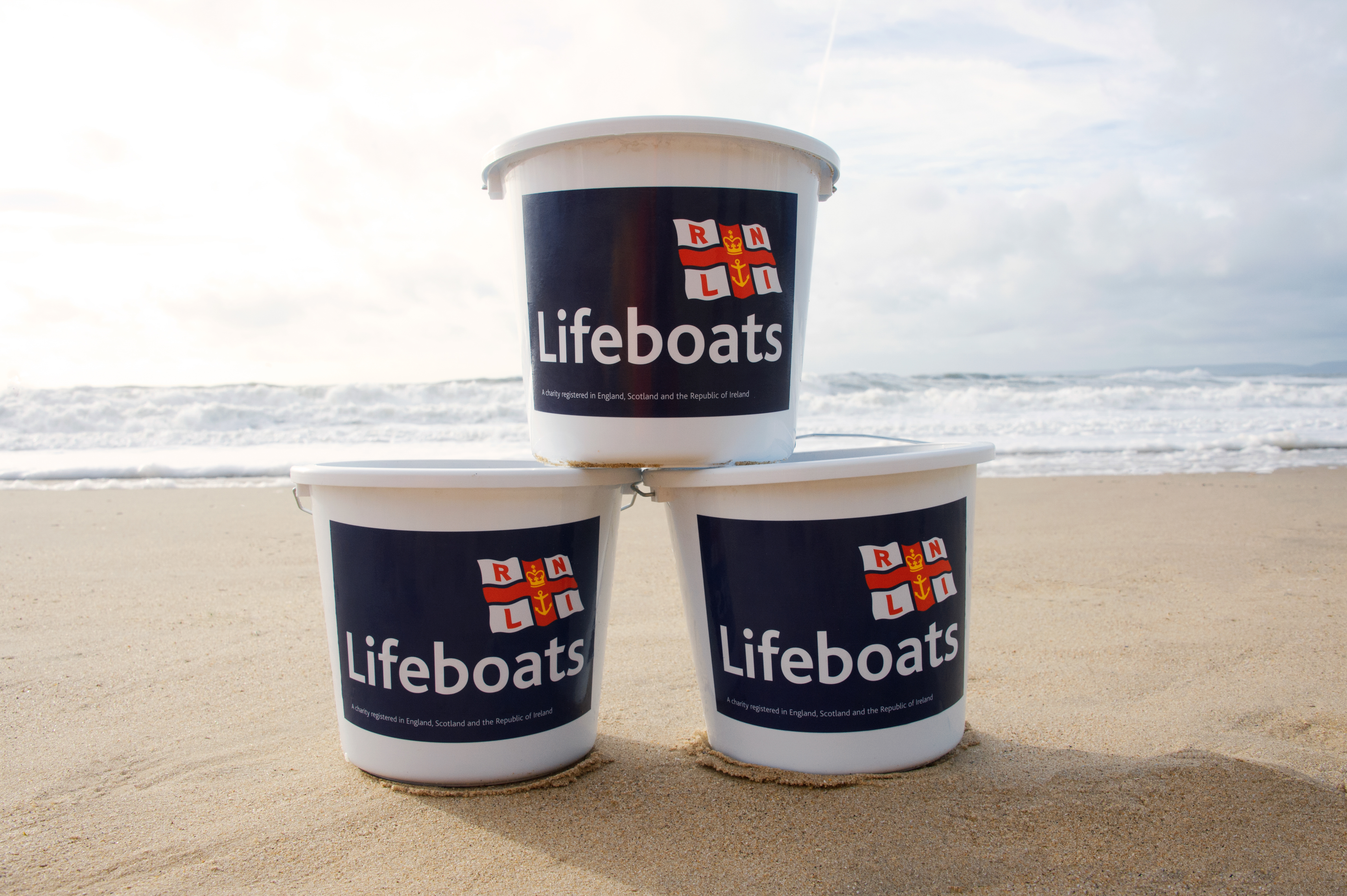 Collection buckets stacked on the beach with sea in background with Lifeboats and RNLI flag on the fronts