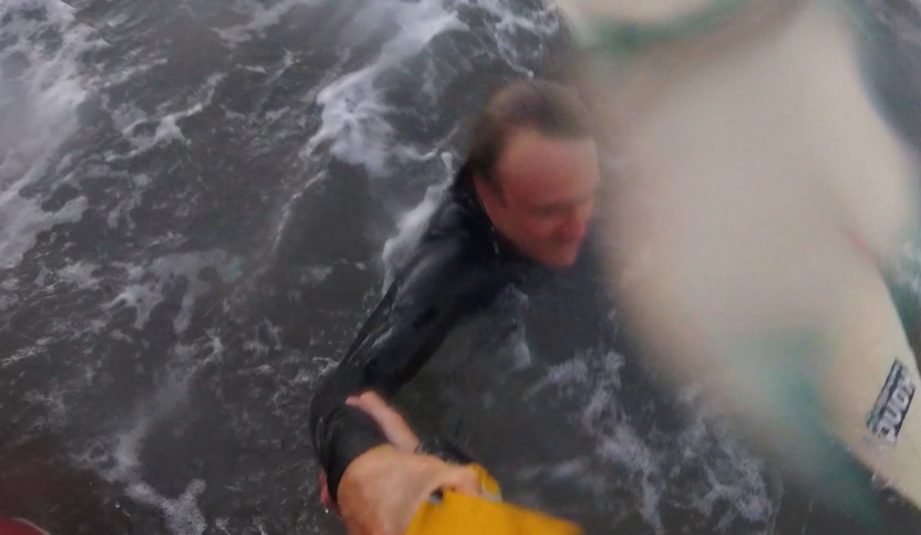 Surfer in water grabbing arm of crew member on lifeboat.